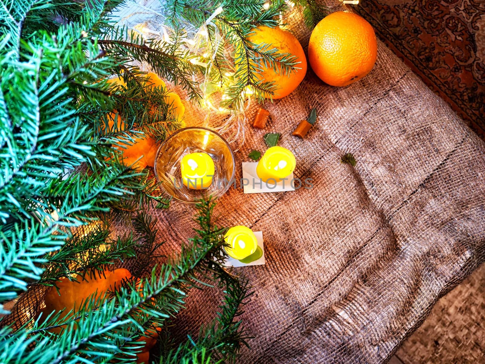 Festive decoration with bouquet and branches of spruce, bright glowing garlands and candles, burlap, oranges. Background for Christmas, New Year. Abstract texture, frame, place for text, copy space