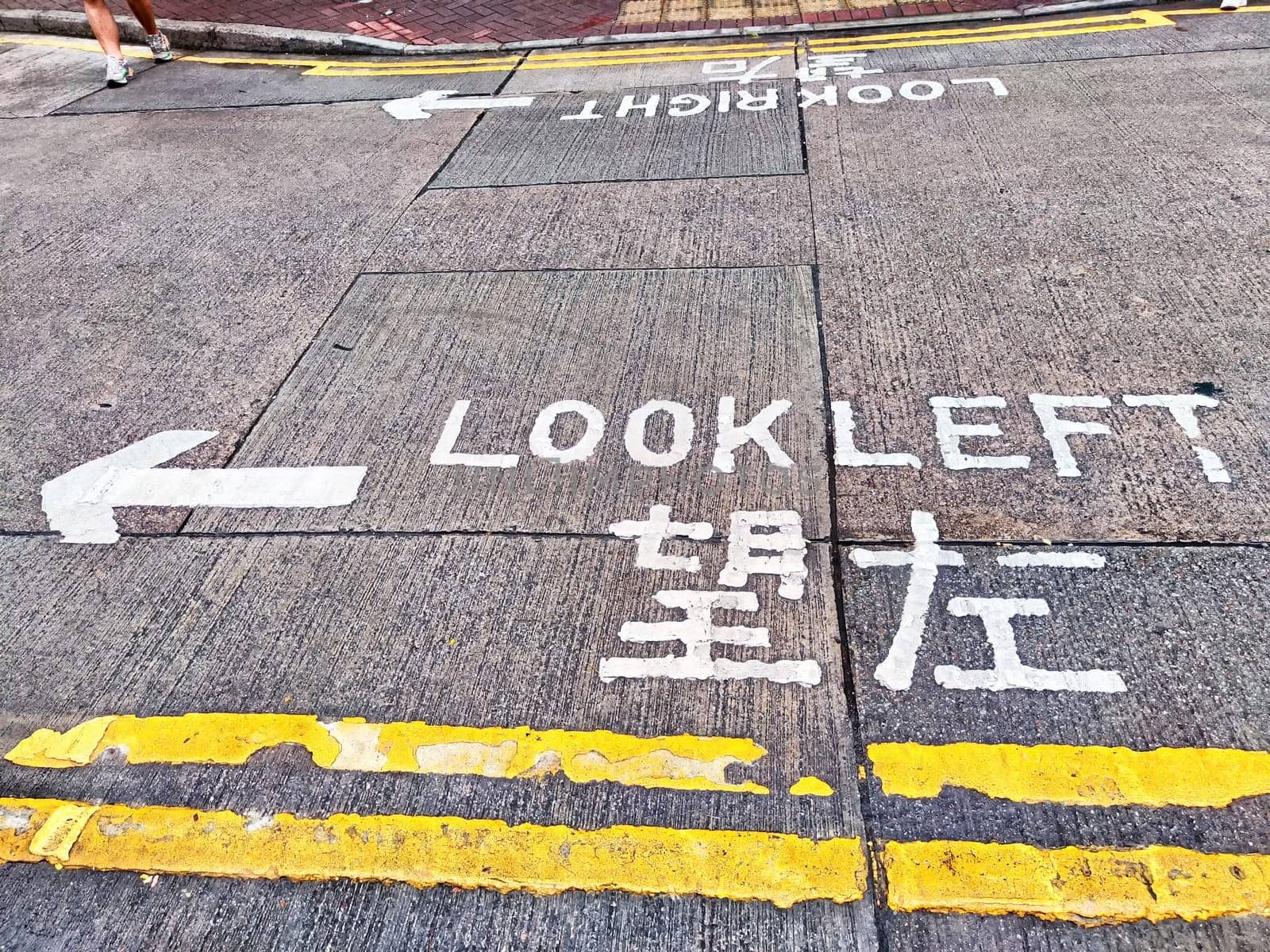 An asphalt road with a pedestrian crossing and sign instructing pedestrians to look left before crossing. Traffic safety