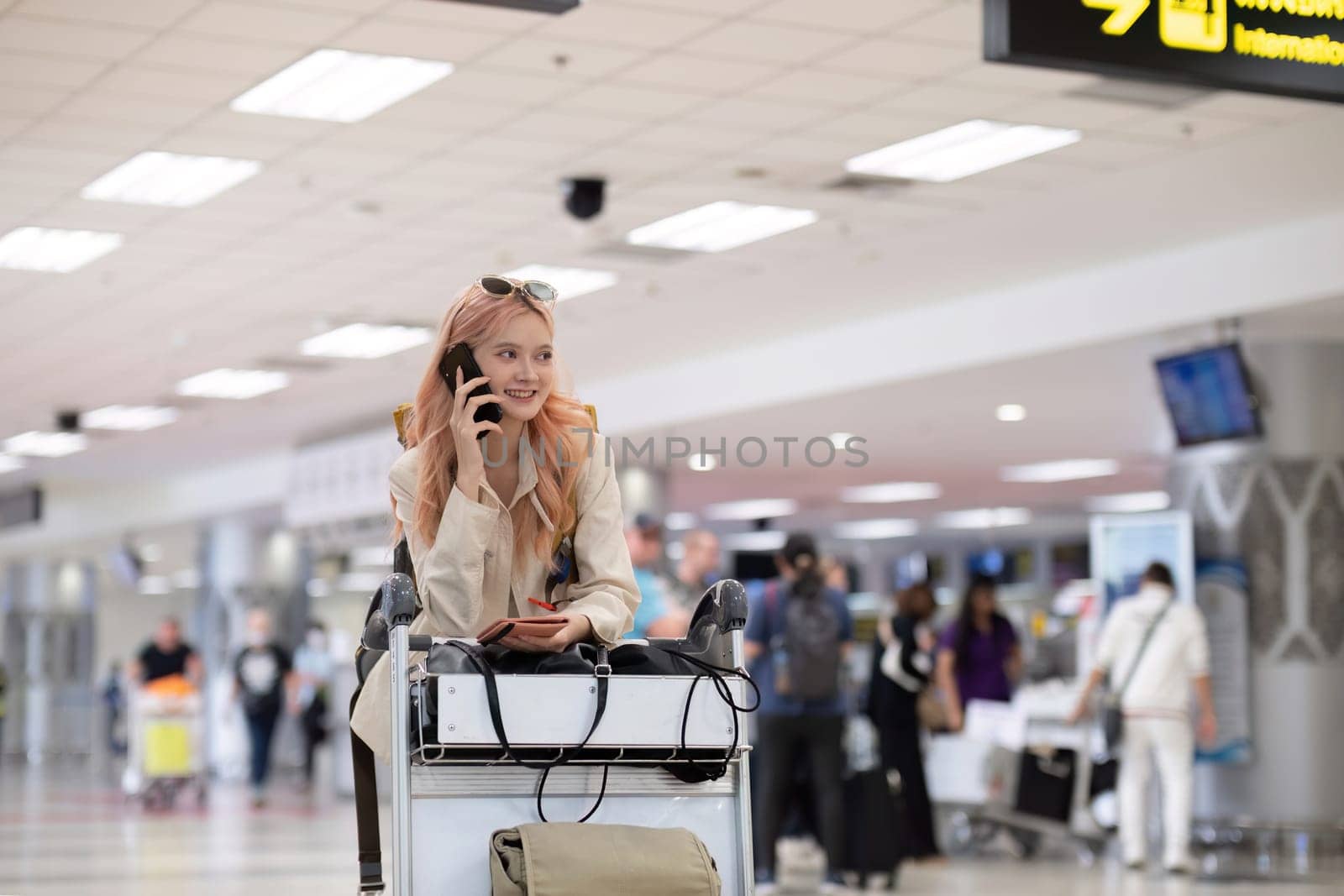 Young woman traveler with pink hair using phone in airport terminal.