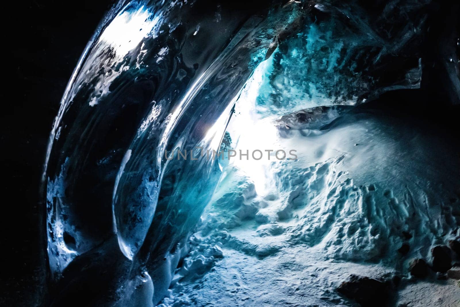 Mesmerizing ice cave amidst the dark landscape of the Bogdanovich Glacier in the Almaty Mountains of Kazakhstan emits a radiant electric blue light, crafting a captivating artwork.