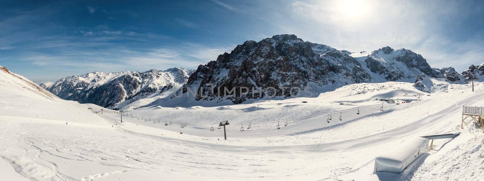 Panorama of ski lift chairs against a backdrop of sunlit mountains on a crisp winter day at high altitude.