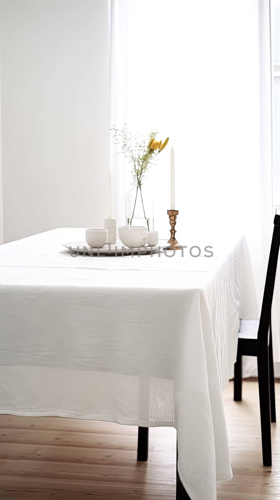 A table with a white tablecloth and a vase of flowers in the center. The table is set with plates, cups, and utensils. Scene is elegant and inviting