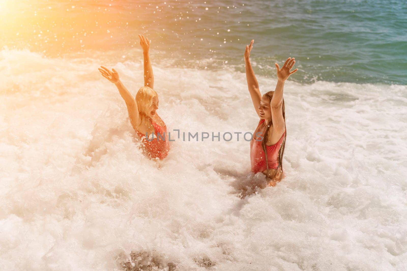 Women ocean play. Seaside, beach daytime, enjoying beach fun. Two women in red swimsuits enjoying themselves in the ocean waves and raising their hands up