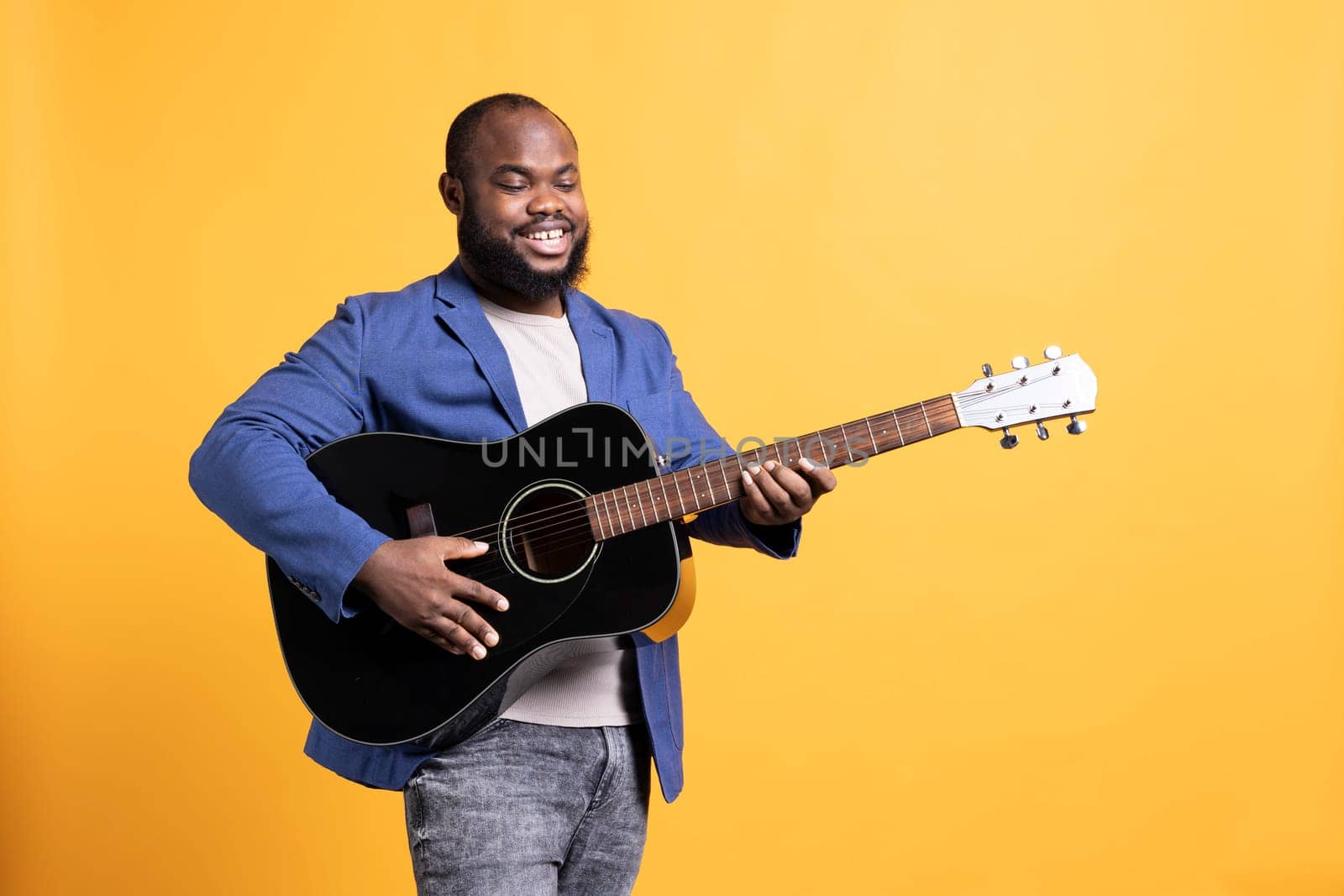 Cheerful man excited to play music on acoustic guitar strings, enjoying hobby, isolated over studio background. Happy musician performing songs on musical instrument, feeling pleased