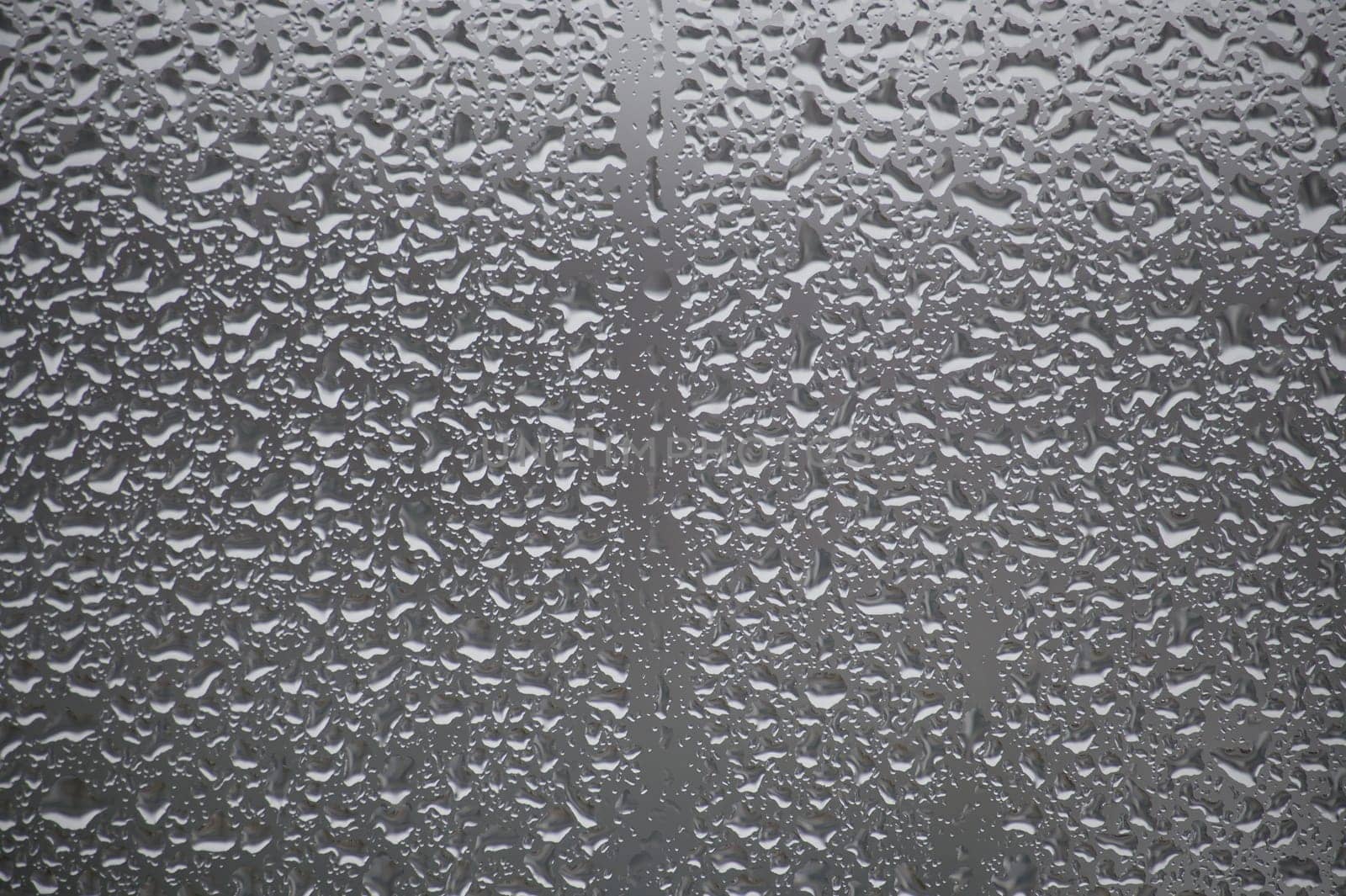 Close-up view of a glass surface covered with many water droplets of various sizes, creating a textured pattern
