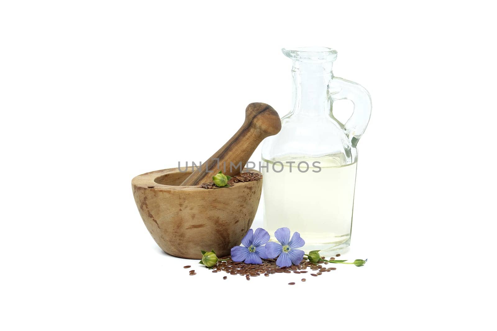 Vibrant blue flax flower is sitting on wooden mortar filled with small brown linseed near linseed oil in glass decanter isolated on white background