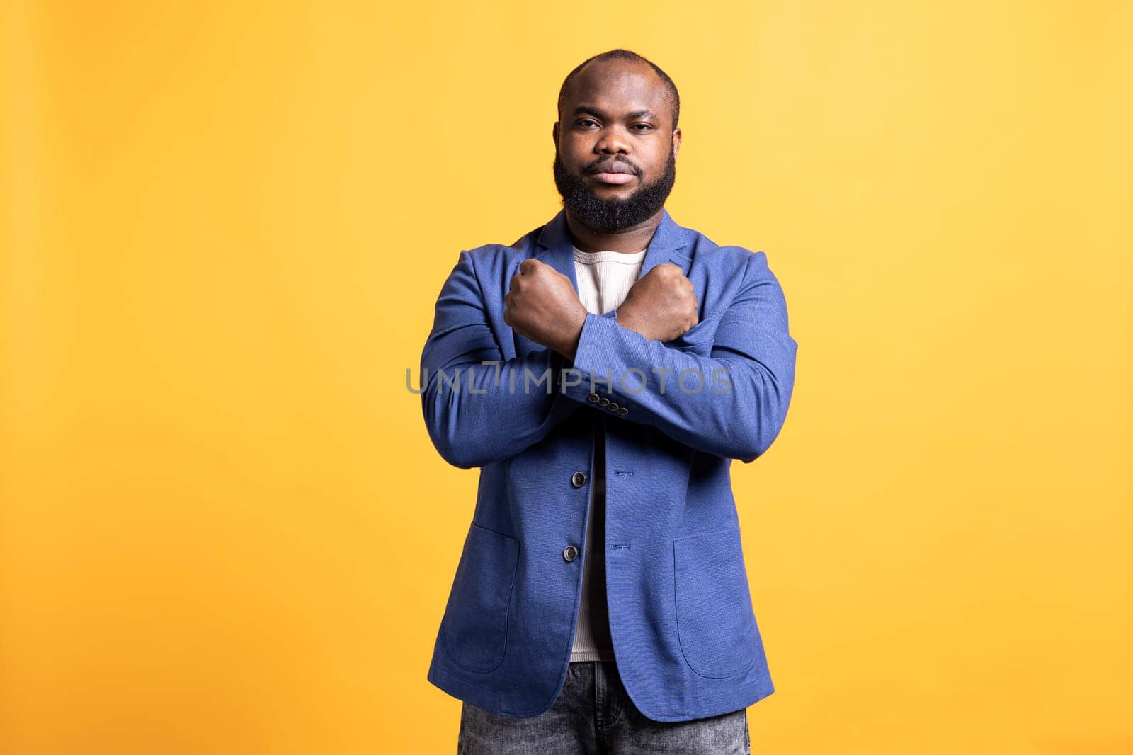 Assertive african american man showing letter X with arms crossed, staying in warrior stance, showing fierceness. Firm BIPOC person using negative body language to signal rejection, studio background