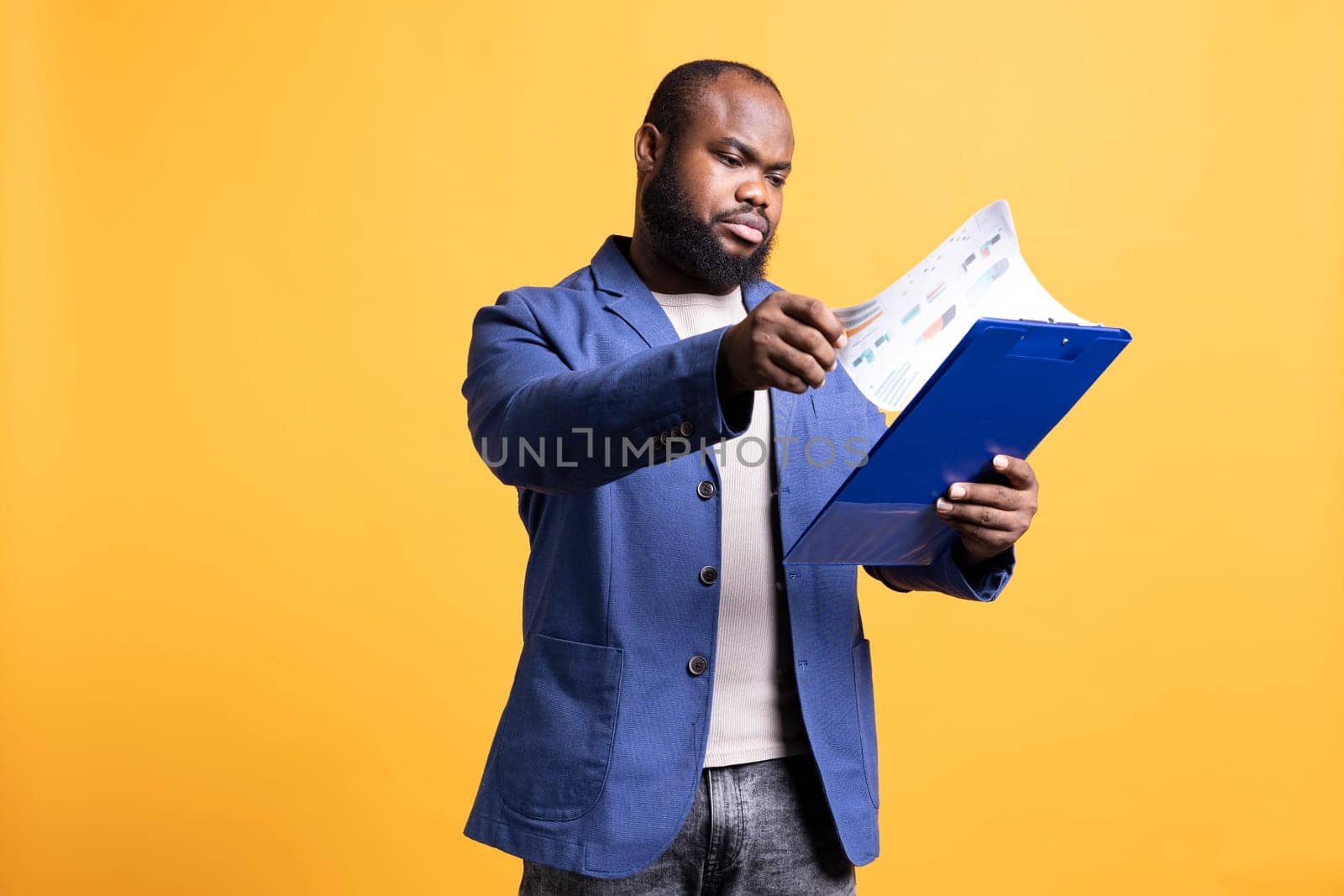 BIPOC person browsing though marketing report pages, studio background. Office clerk reading clipboard with documents containing economic graphs and figures, solving business tasks