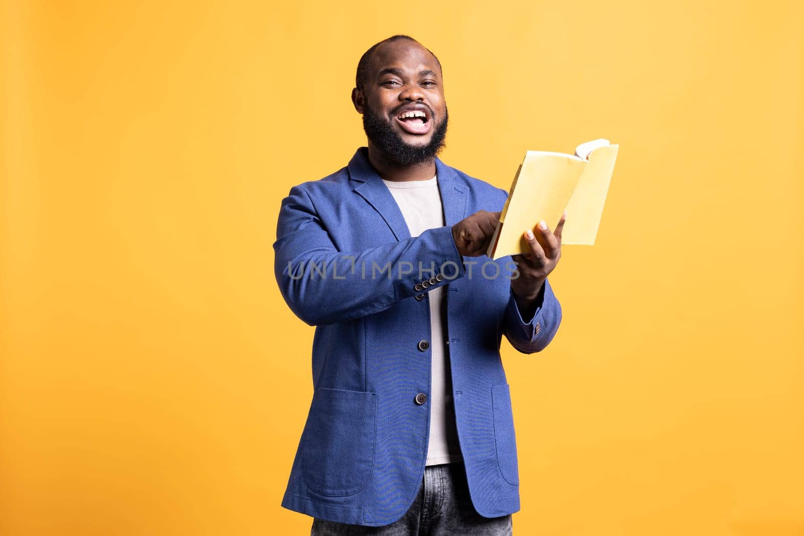 Man laughing while reading funny book, entertained by engrossing story. Happy person having fun, being amused by literature novel during leisure time in studio background