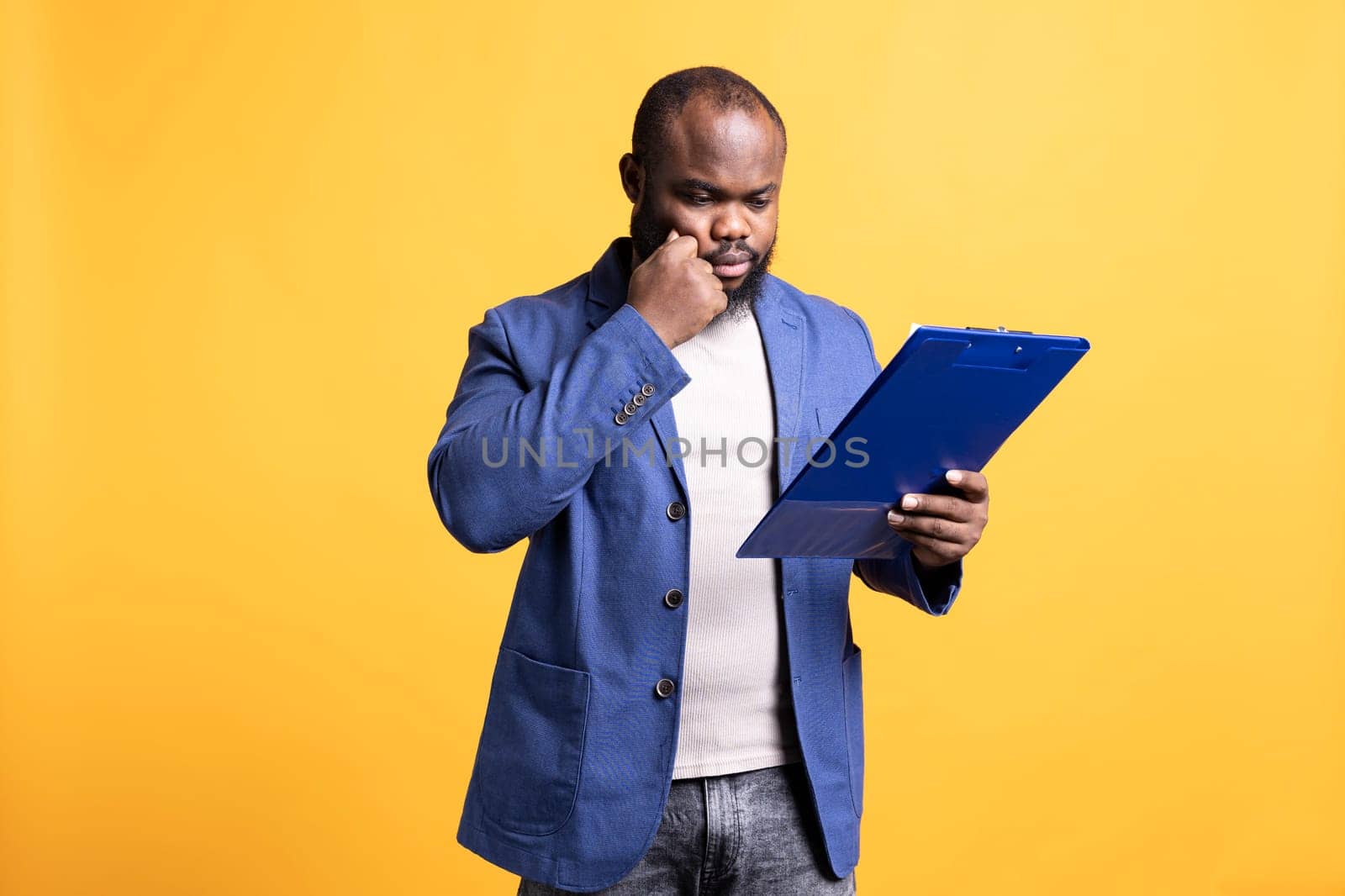 African american man browsing though financial report pages, isolated over studio background. Worker reading clipboard with files containing economic graphs and figures, solving business tasks