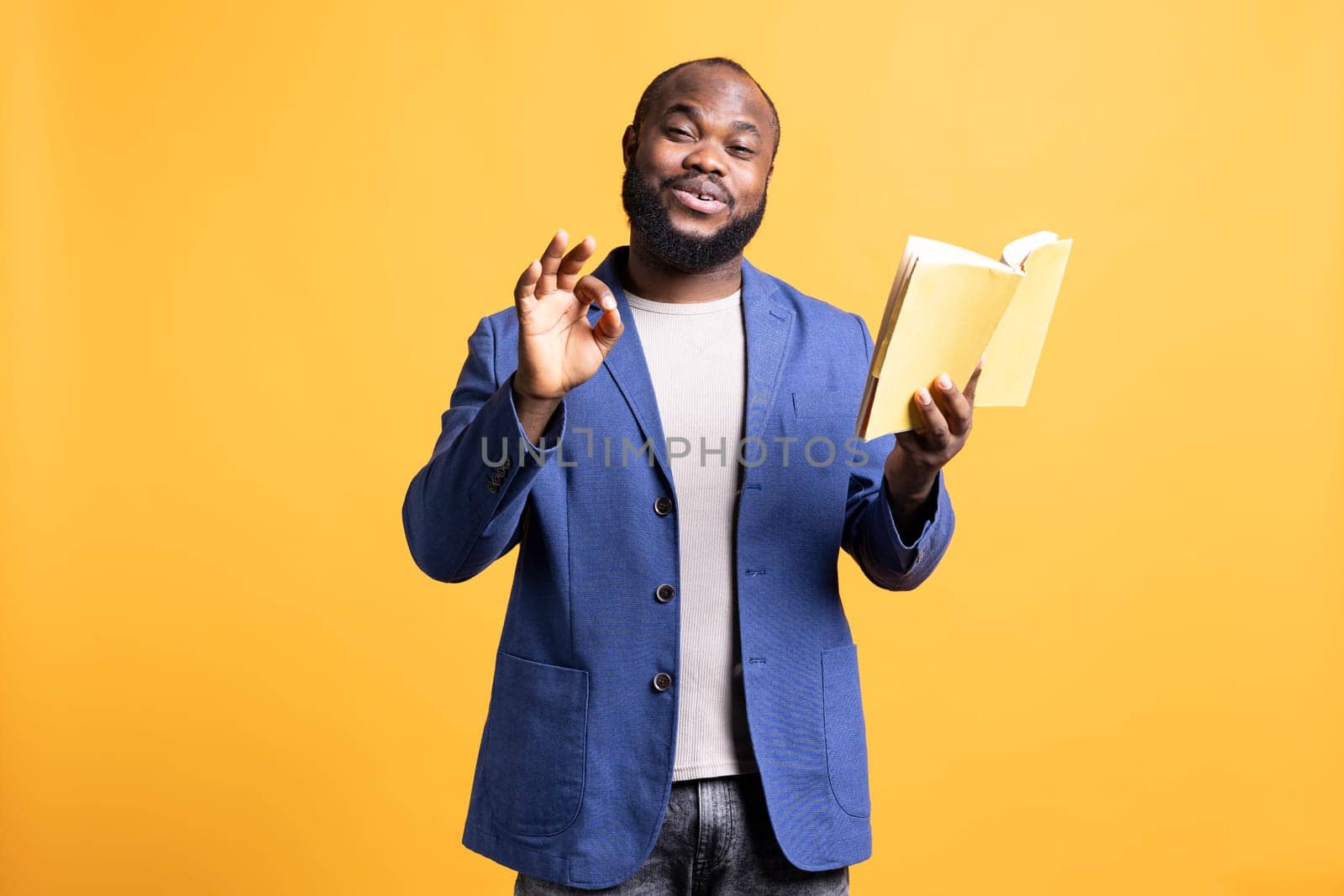 Portrait of jolly african american man recommending interesting book after being entertained by well written story. Joyous person showing positive hand gesturing, enjoying novel, studio background