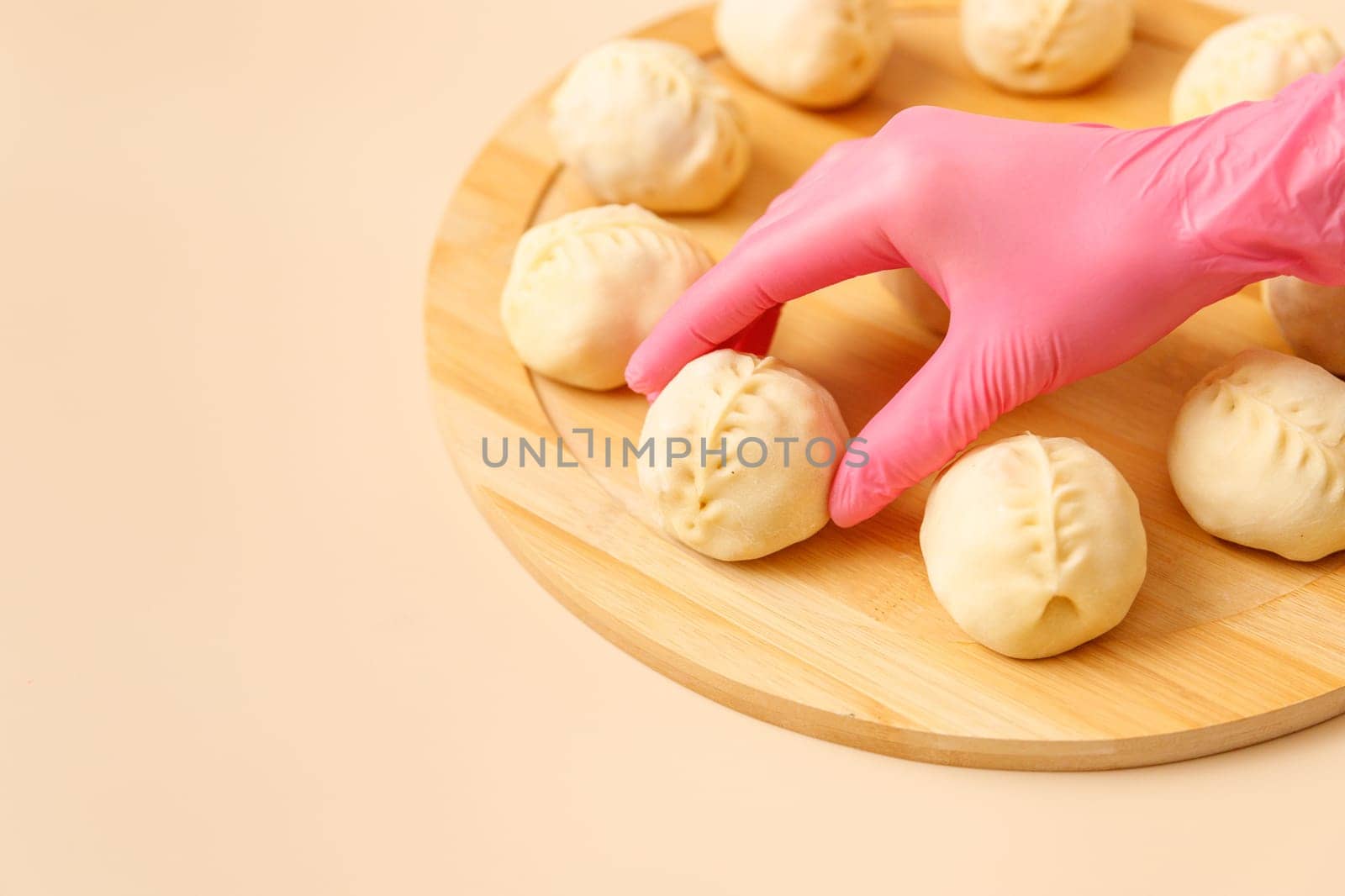 Close-up of skilled chef's hand in rubber glove arranging traditional Central Asian manty with meat on wooden board, frozen semi-finished products, copy space.