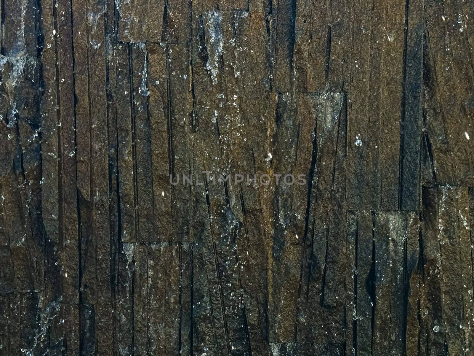 Close up of textured dark brown stone tiles with water drops. Detailed nature photography capturing intricate patterns. Natural background. High quality photo