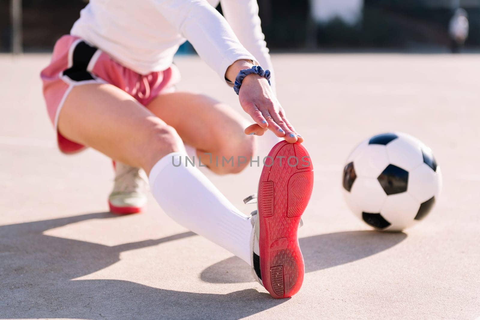 unrecognizable woman with a soccer ball stretching legs in a football court, concept of sport and active lifestyle