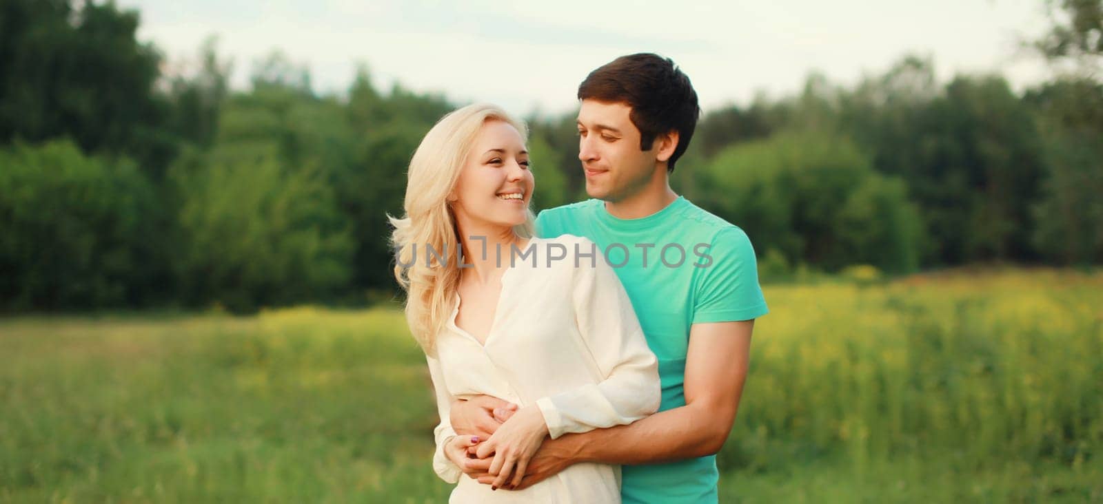 Portrait of beautiful happy smiling young couple in love together hugging in green summer park