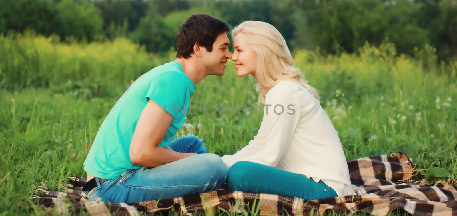 Portrait of beautiful happy smiling young couple in love lying together on the grass looking at each other having a picnic, summer park