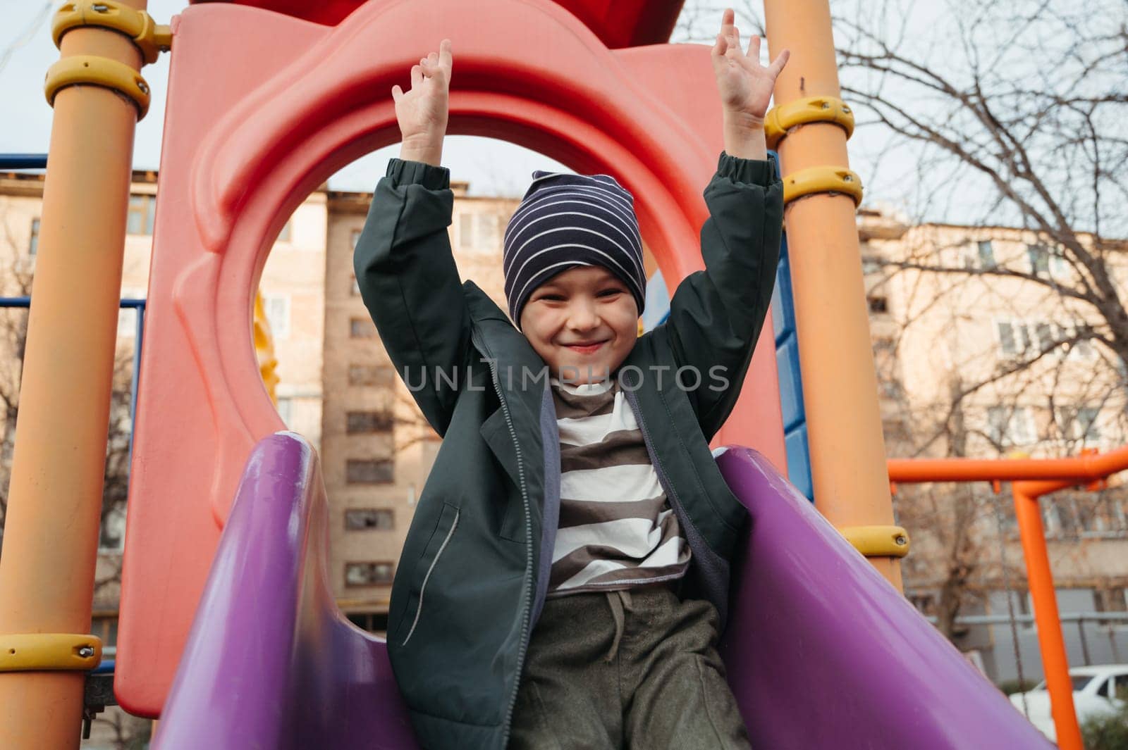 happy baby child boy rides a slide on the playground in autumn