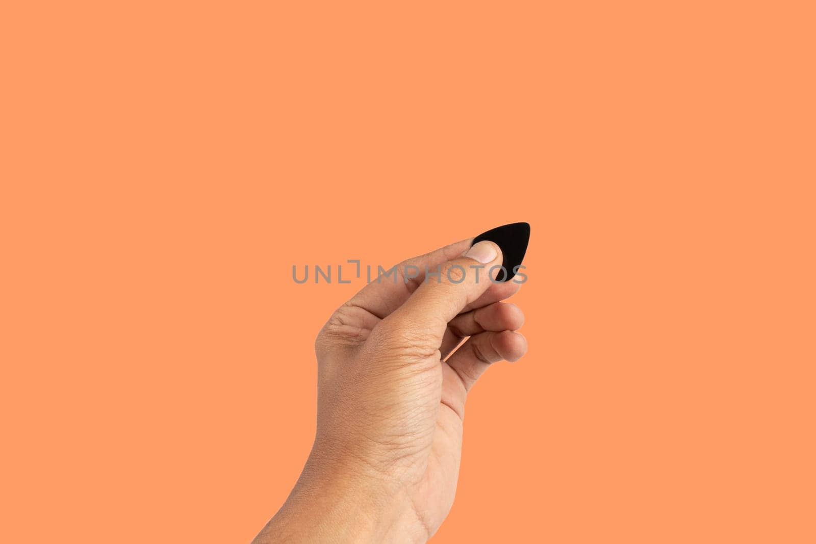 Black male hand holding a guitar pick isolated on orange background. High quality photo