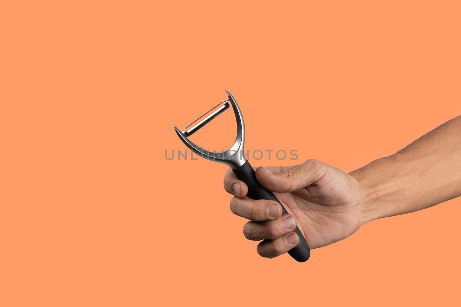 Black male hand holding a potato peeler isolated on orange background. High quality photo