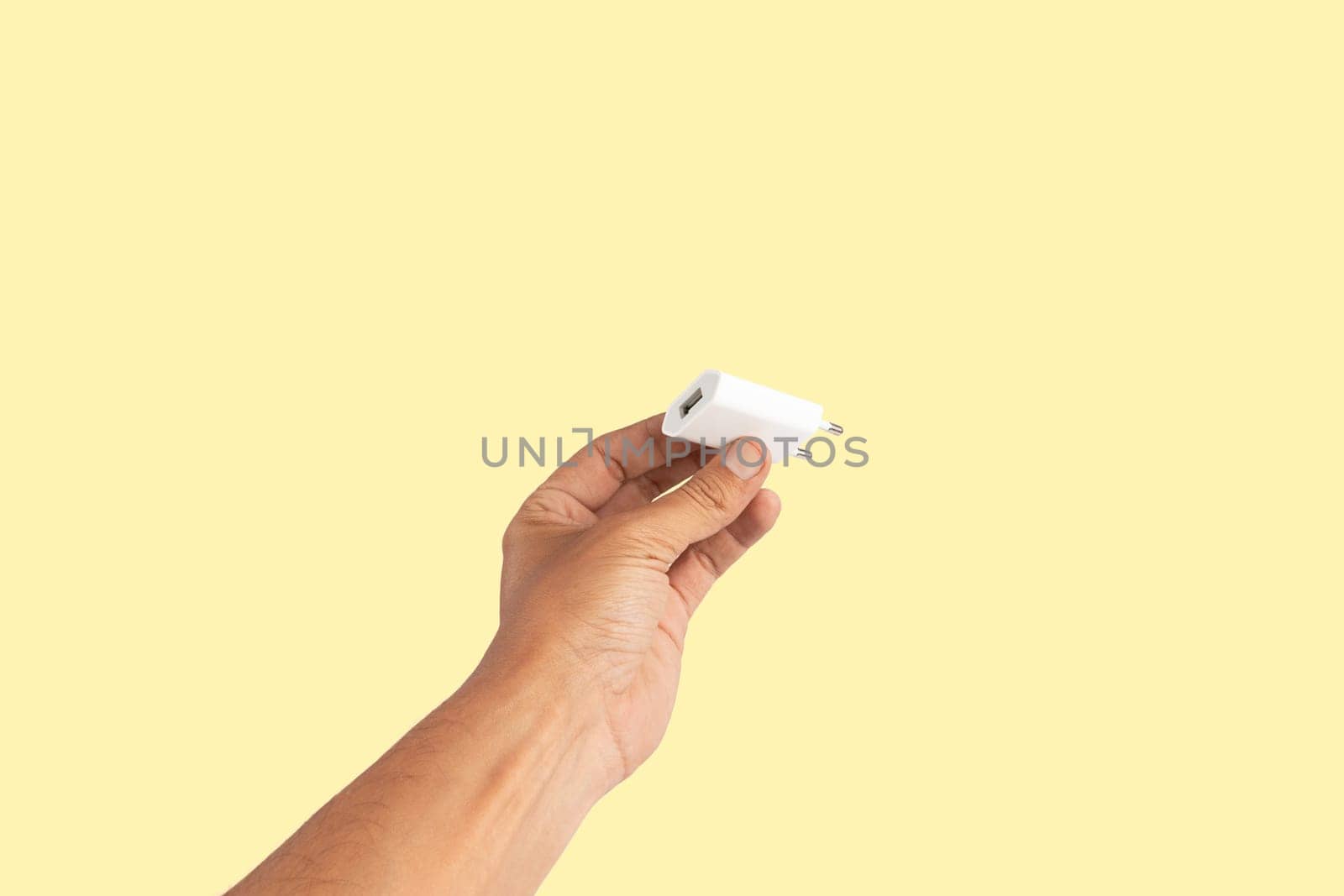 Black male hand holding a USB charger plug isolated on yellow background. High quality photo