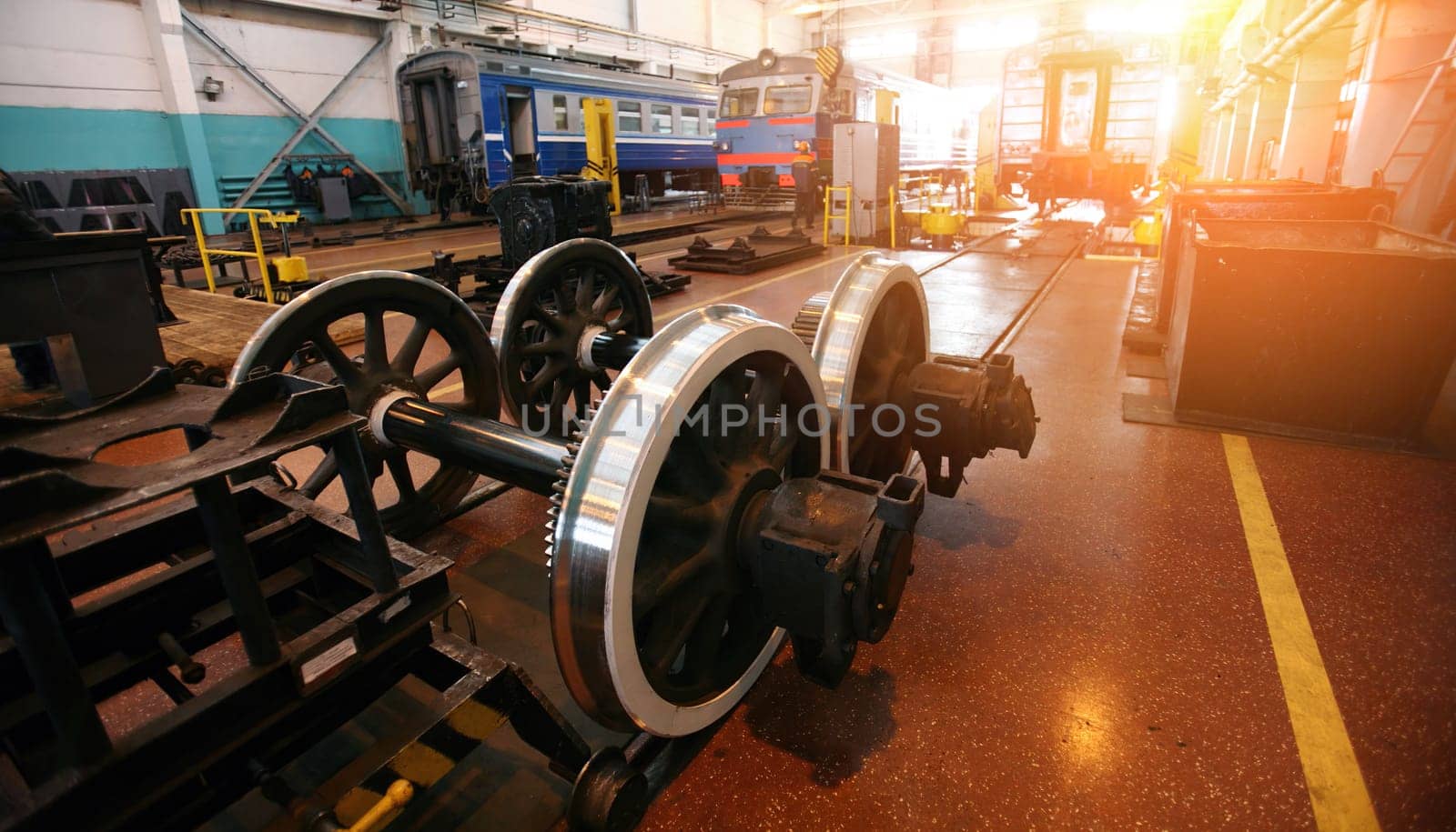 The workshop showcases the maintenance of railway equipment with a focus on a locomotive and a set of gleaming train wheels. Workers are possibly present, tending to the overhaul and repair of these vital components that keep the transportation network running smoothly. The setting suggests routine upkeep, keeping safety and efficiency at the forefront.