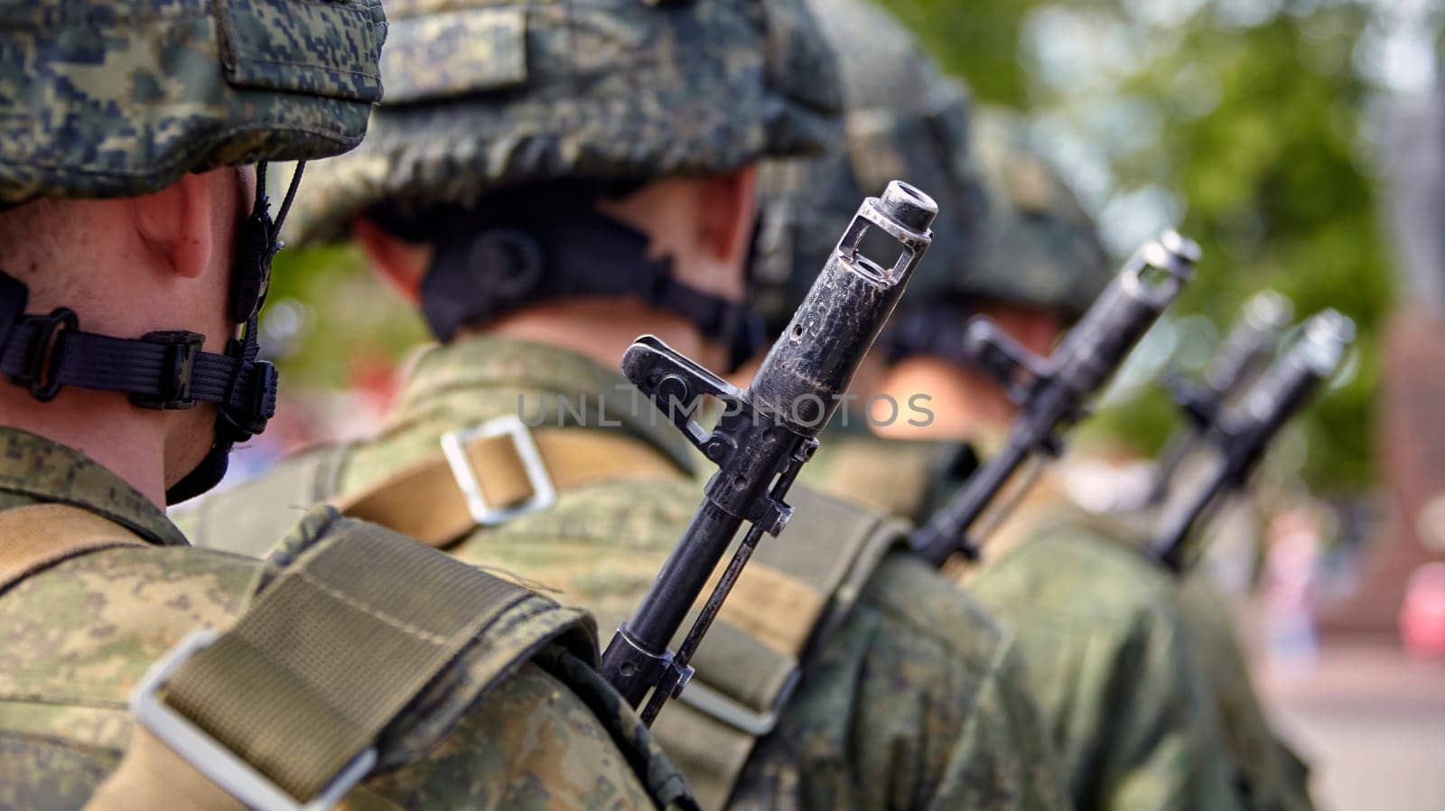 A soldier in full gear stands at attention with a rifle, wearing a helmet and camouflage uniform. Blurred background adds focus and determination to his readiness and vigilance.
