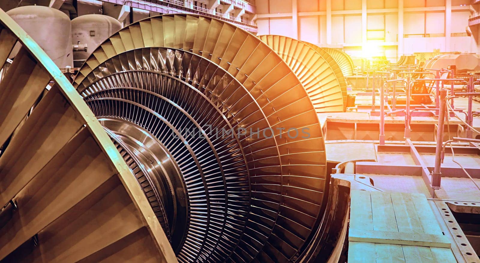 A close-up view of a large turbine blade inside a power plant, bathed in the warm light of the afternoon sun. The intricate design of the blades is highlighted, showcasing the complex engineering involved in generating power.
