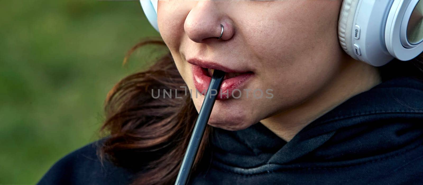 A close-up shot of a young woman wearing headphones, biting on a straw. Her face is relaxed, suggesting a moment of peace and quiet.