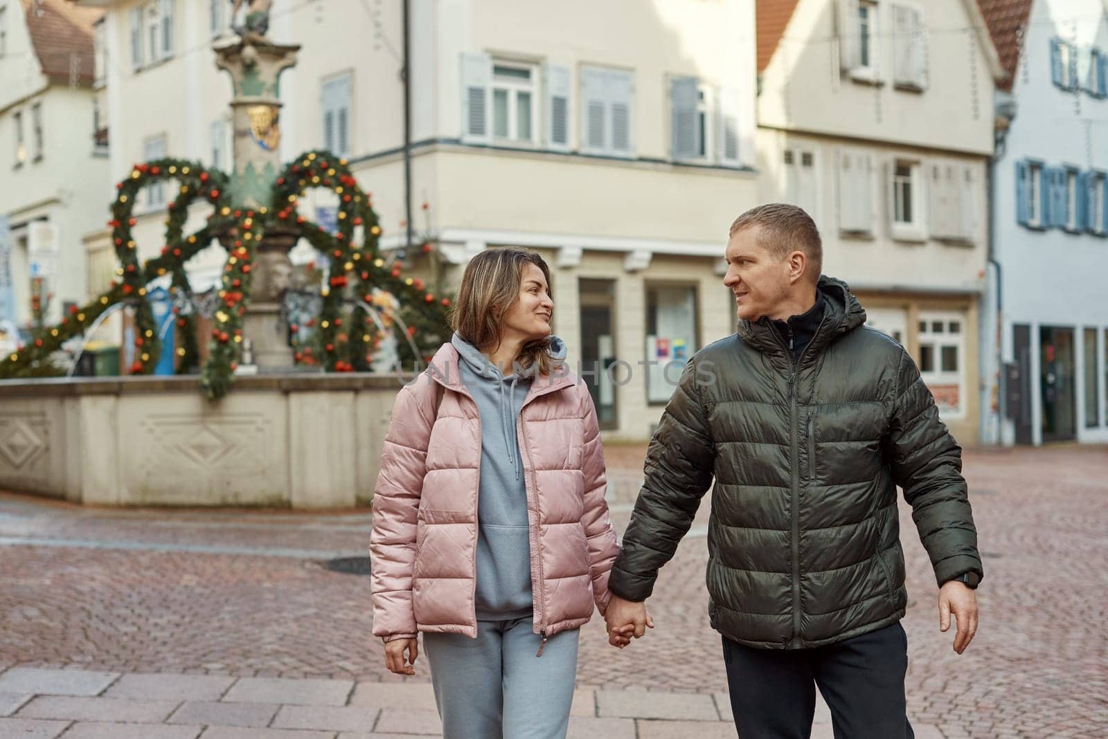 Loving couple of tourists walking around old town. Couple of lovers leisurely stroll in the cool autumn morning on the streets of a BIETIGHEIM-BISSINGEN (Germany). The guy holds his wife. Vacation, Winter, holiday. Romantic Stroll through Historic German Charm. Couple Walking in Europe's Old Town by Andrii_Ko