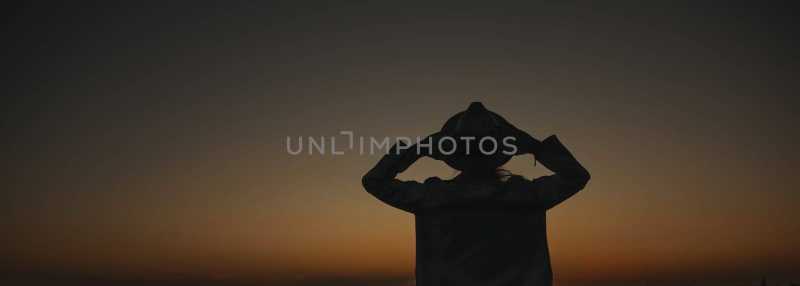 A woman is standing in the dark with her arms outstretched, looking up at the sky. The sky is a deep blue color, and the sun is setting. The woman is lost in thought