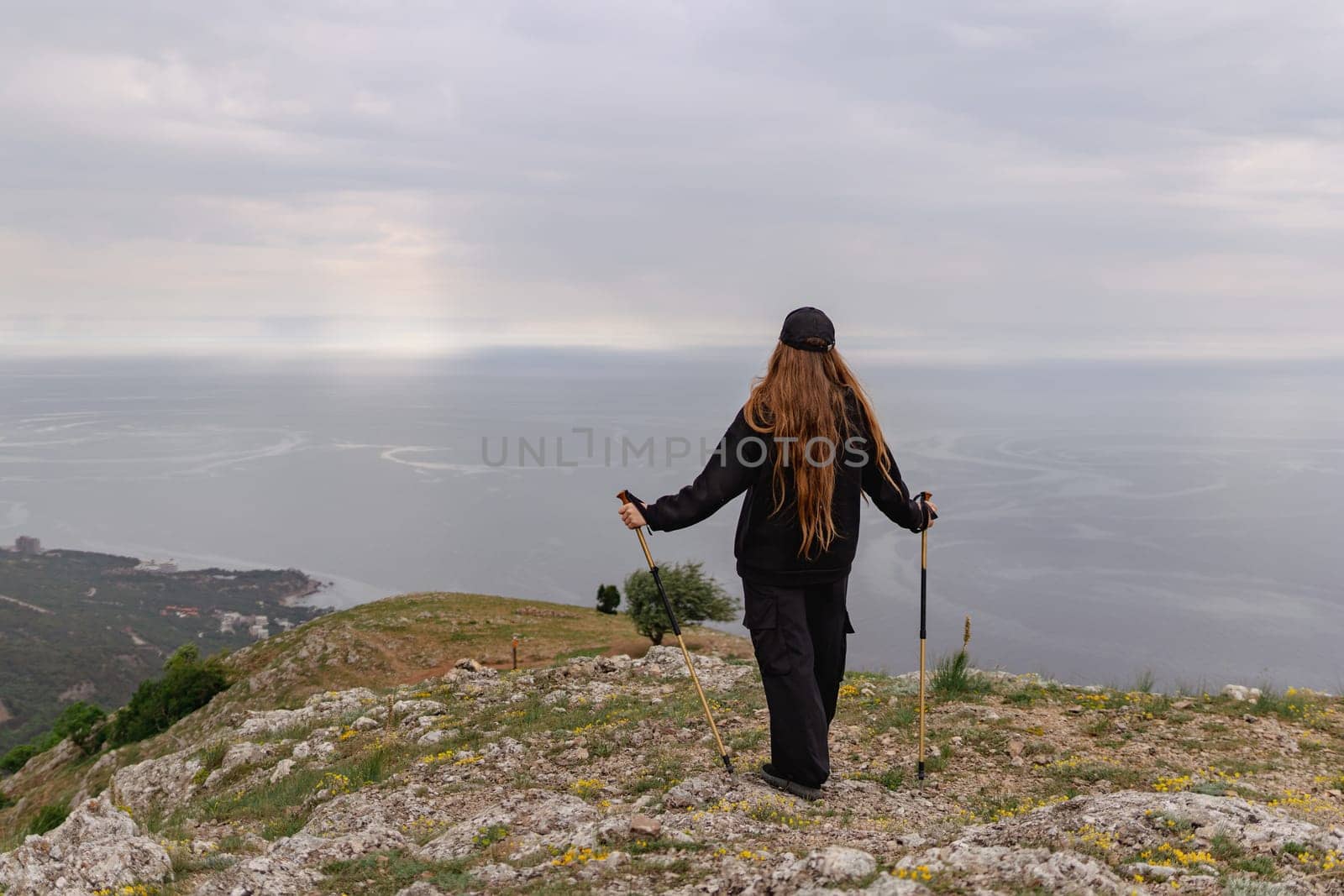 A woman with long hair is standing on a hill overlooking the ocean. She is holding two poles and she is enjoying the view