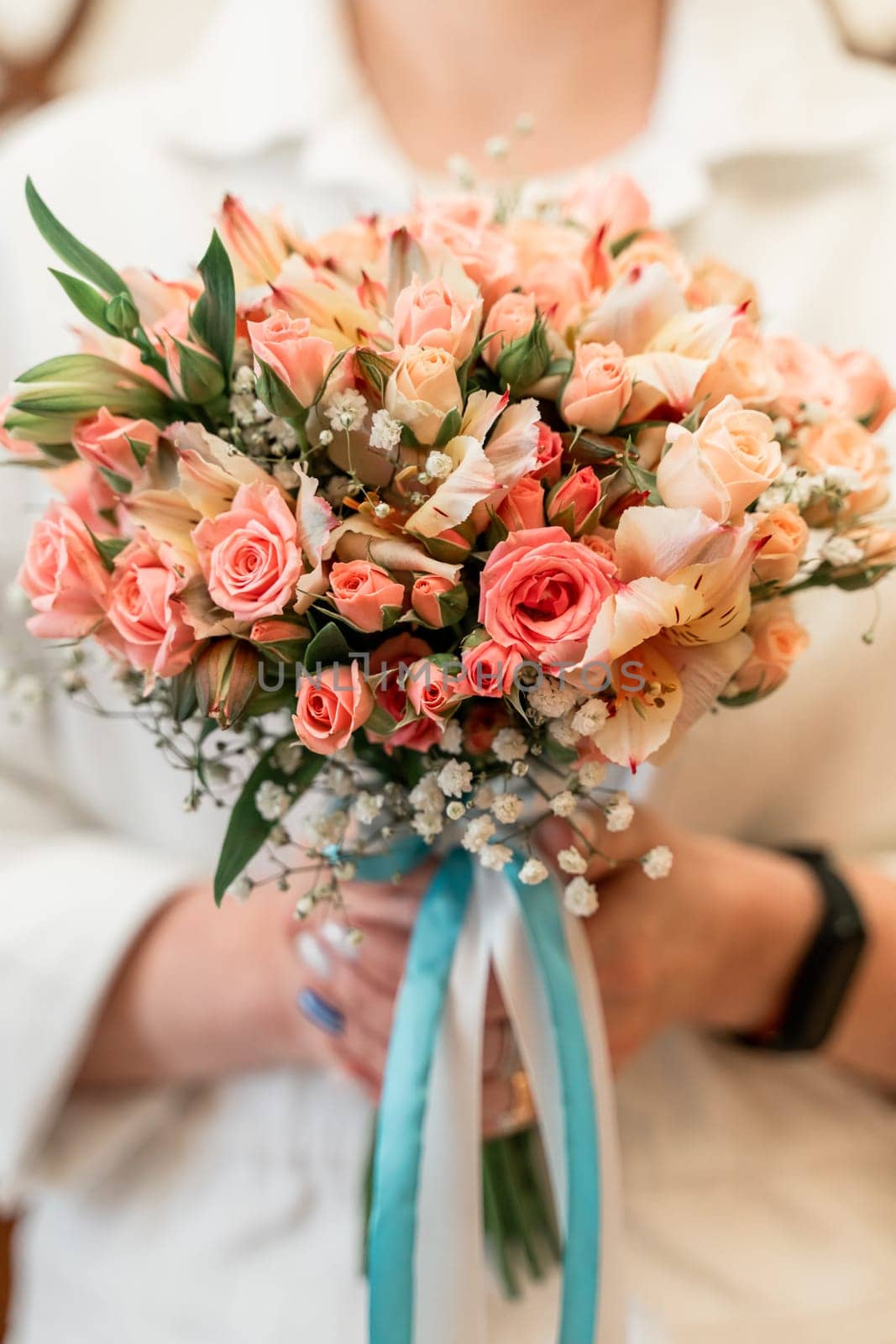 A woman is holding a bouquet of pink flowers with white accents. The bouquet is tied with a blue ribbon