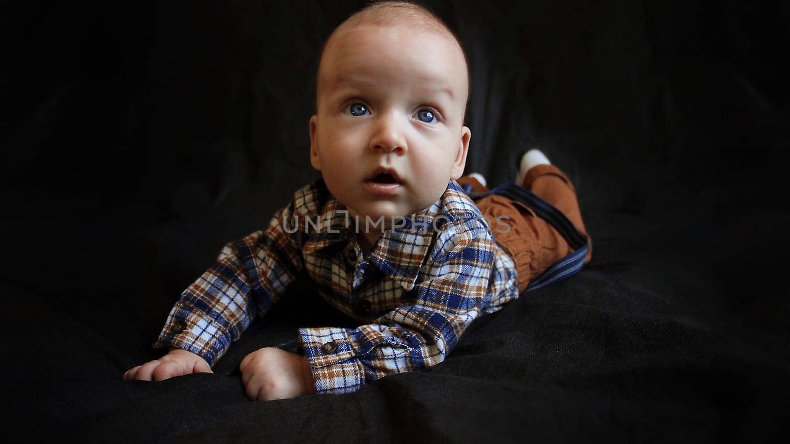 A kid in mustard pants and a plaid shirt lies on a black background. High quality photo