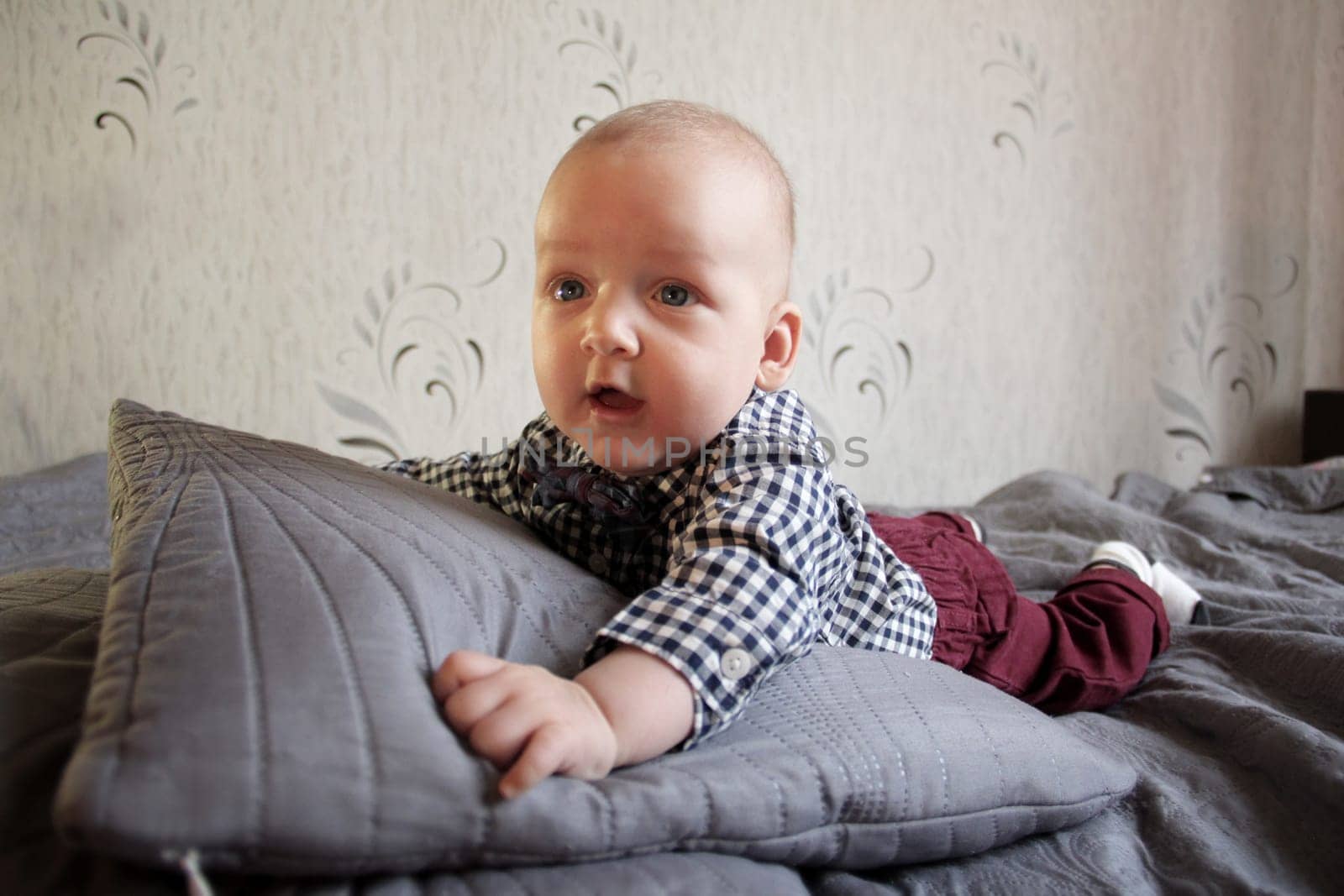 A baby in a plaid shirt and maroon pants lies on the bed by VeronikaAngo