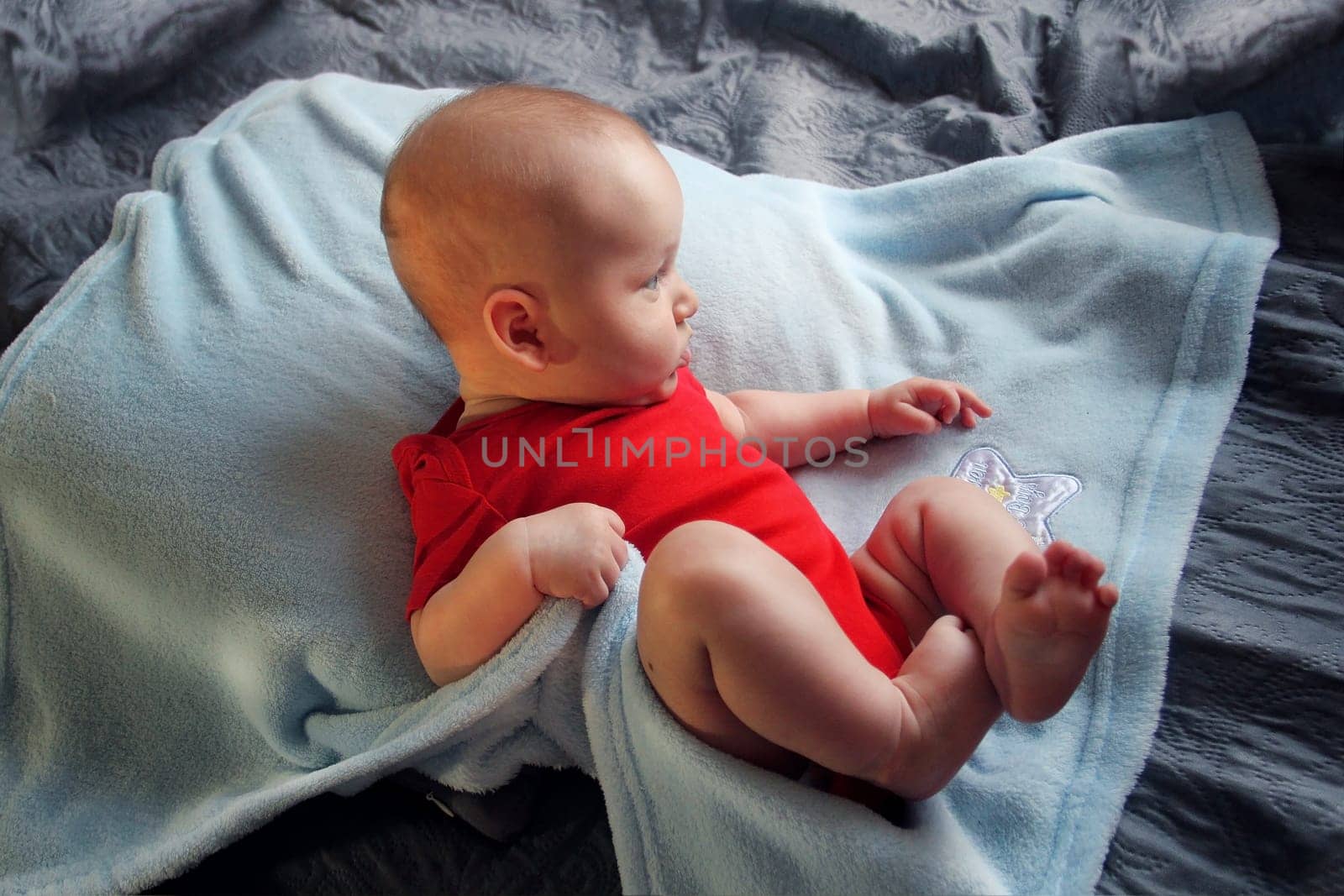 Baby in a red bodysuit lying on a blue blanket. High quality photo