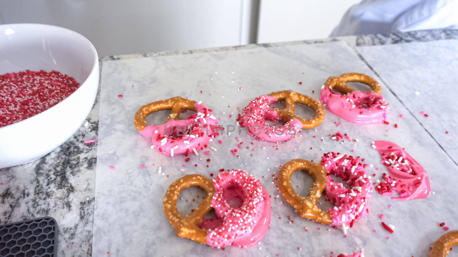 Freshly dipped and still glistening, these crunchy pretzels are lovingly adorned with pink chocolate and a scattering of colorful sprinkles, promising a feast for the senses.