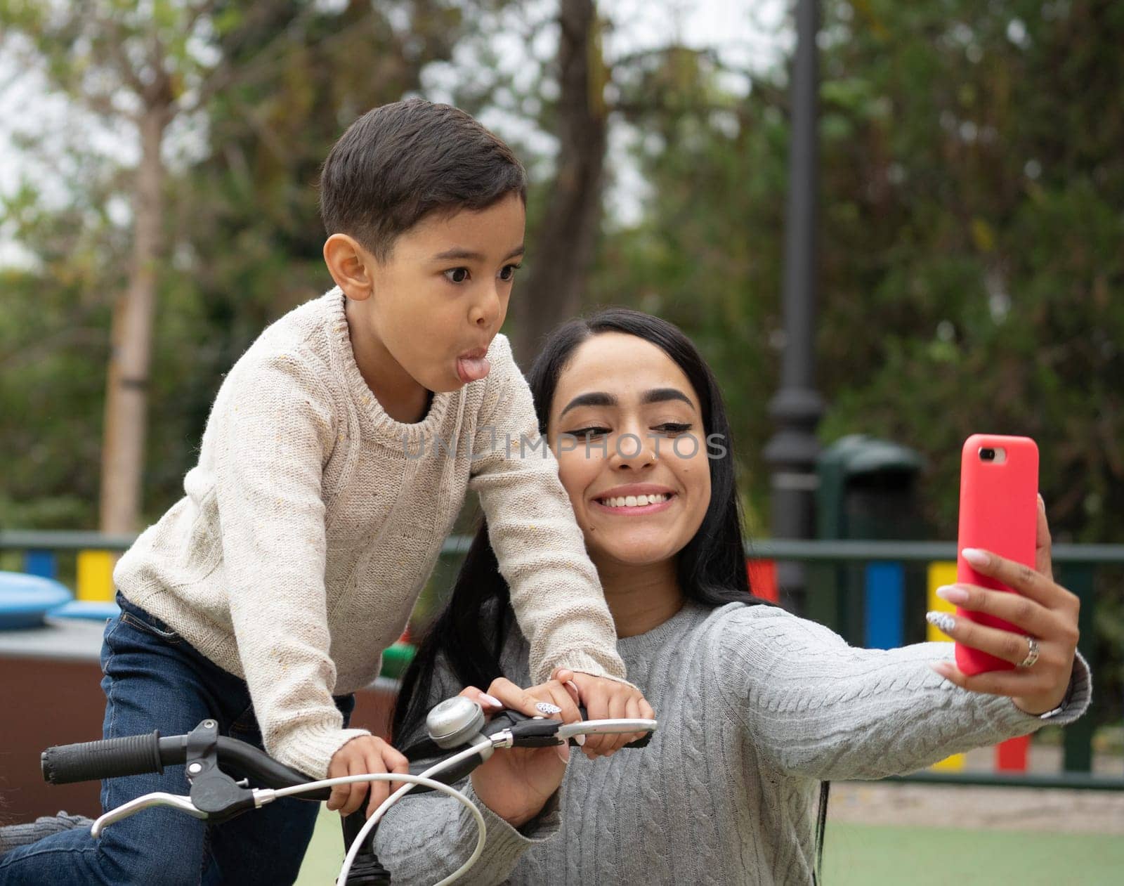 Latin single mother family taking a funny selfie in a park outdoors.