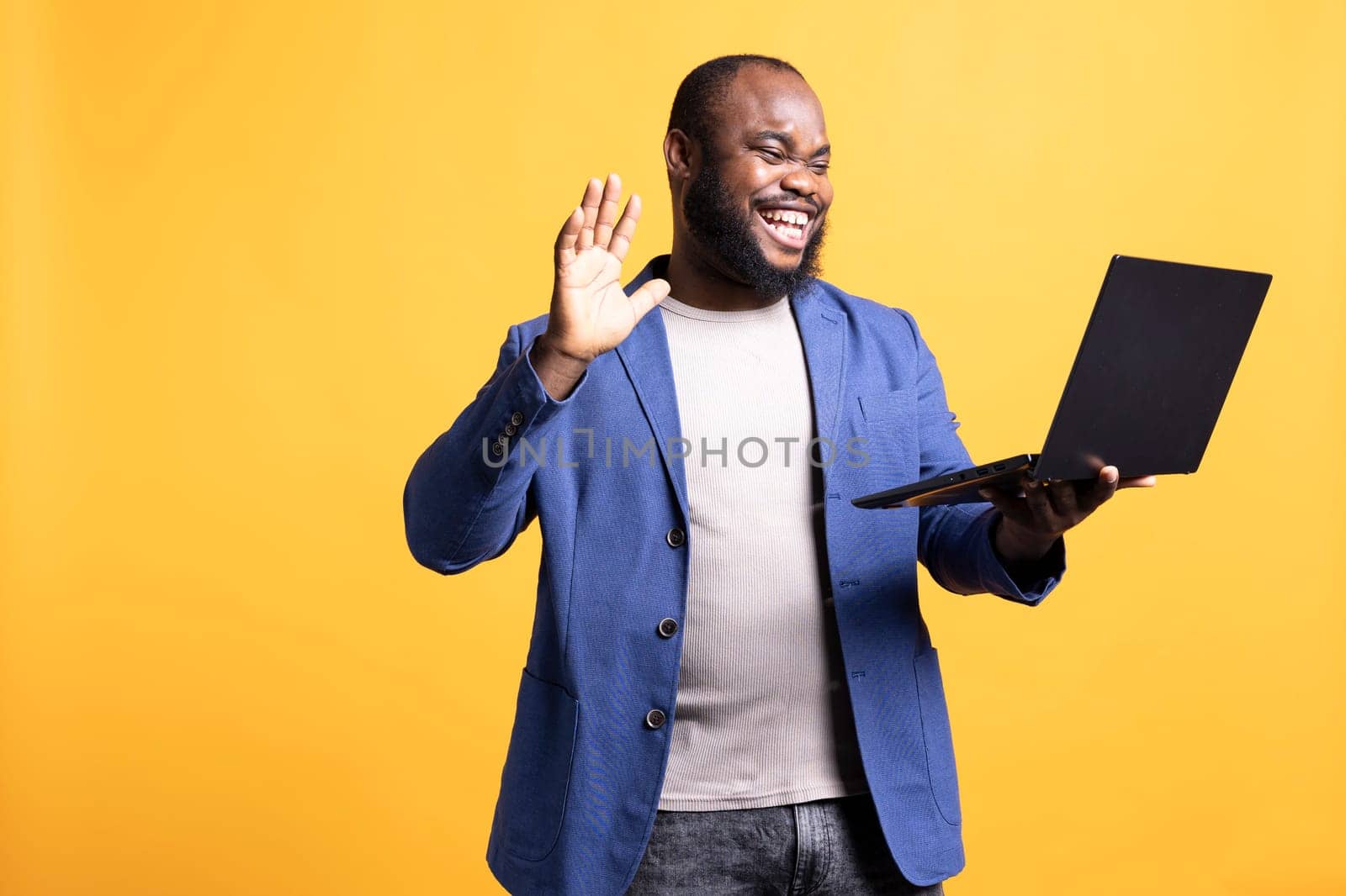 Joyful african american man greeting coworkers during teleconference meeting, isolated over studio background. Happy worker waving hand, saluting colleagues during internet video call