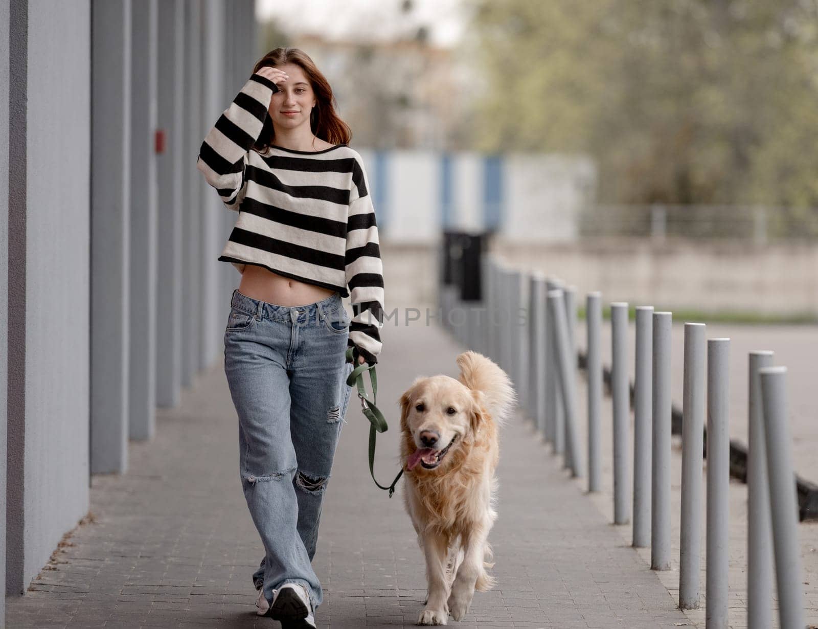 Teenage Girl Walks With Golden Retriever In City During Spring