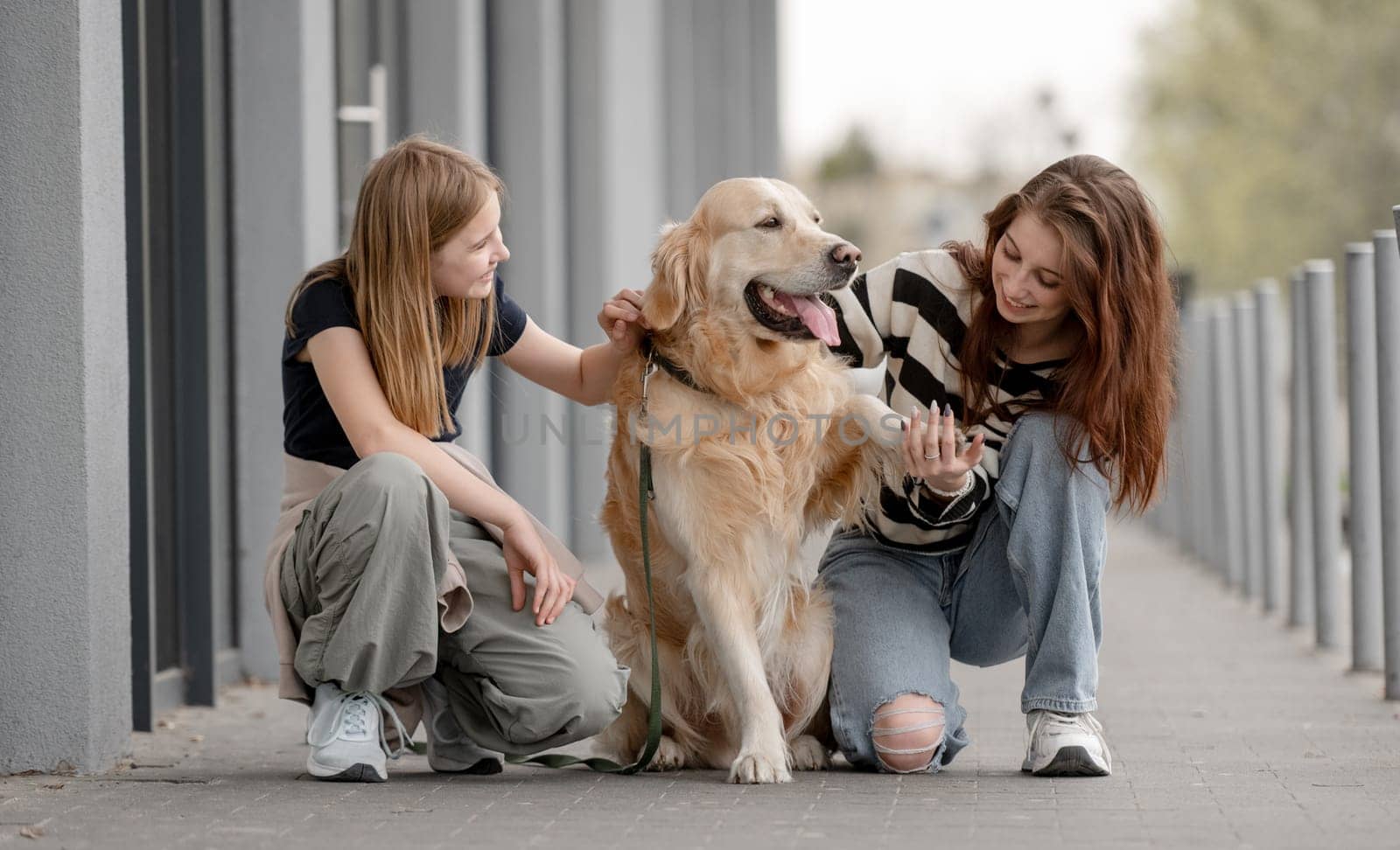 Two Girls With Golden Retriever Sitting And Playing Outside In Spring
