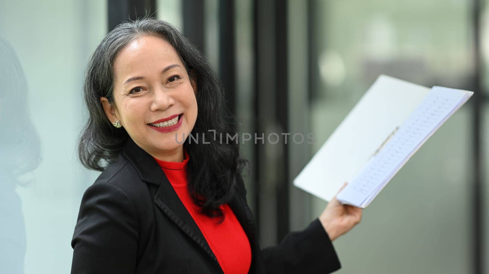 Attractive mature businesswoman holding documents and smiling confidently at camera.