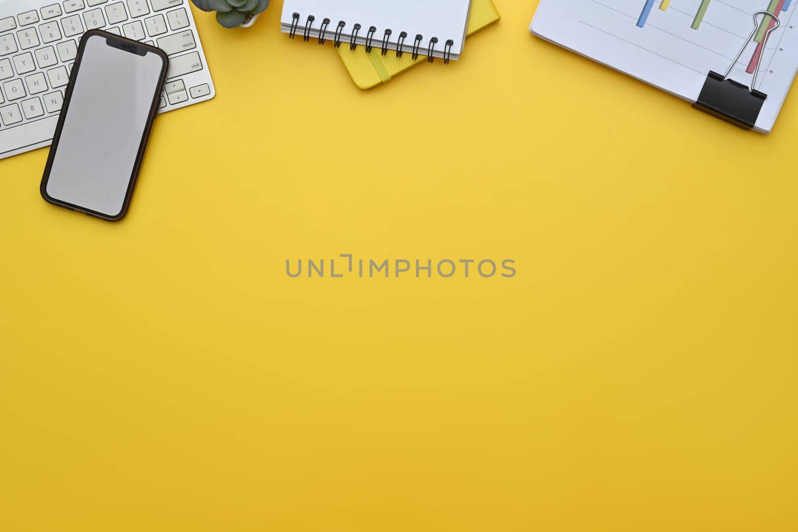 Smartphone, keyboard, notepad and financial documents on yellow background.