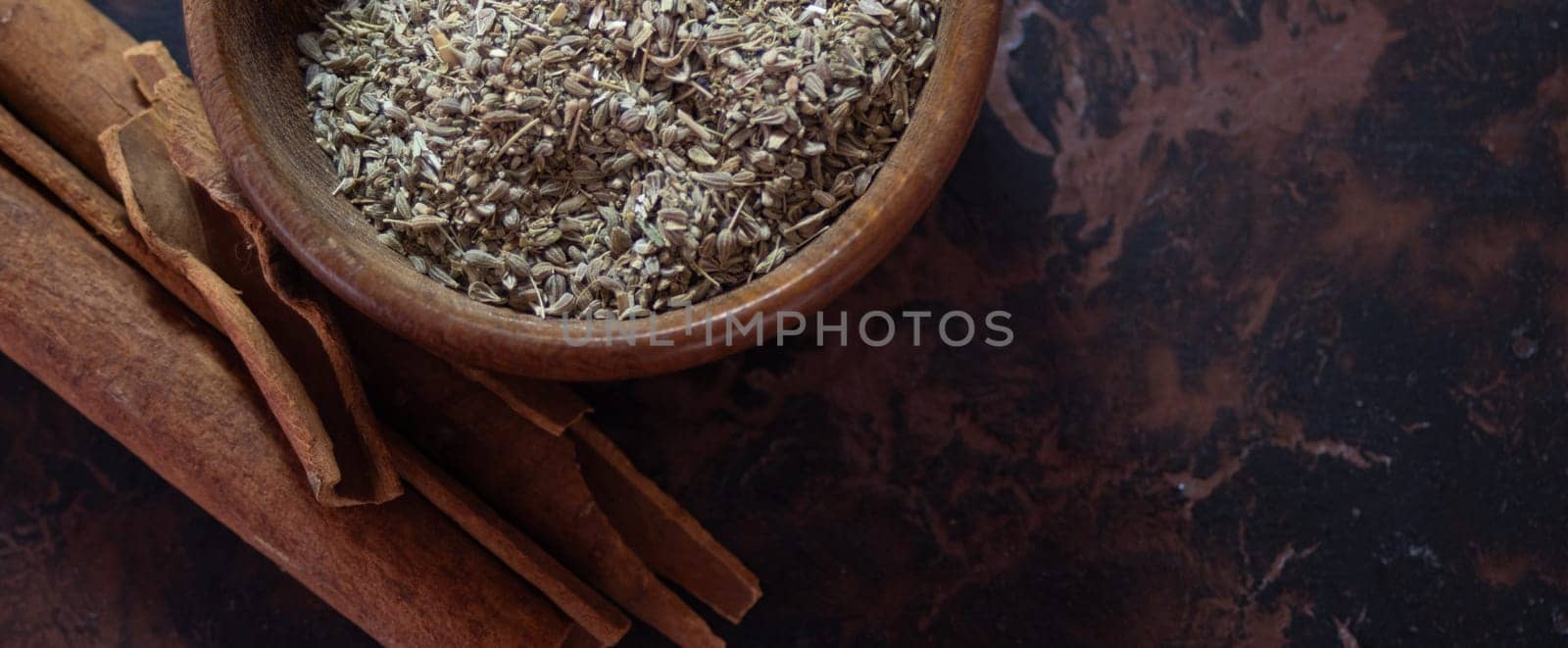 Brown wooden background.. Horizontal picture. Still life. Wooden bowl with anise seeds and cinnamon sticks.