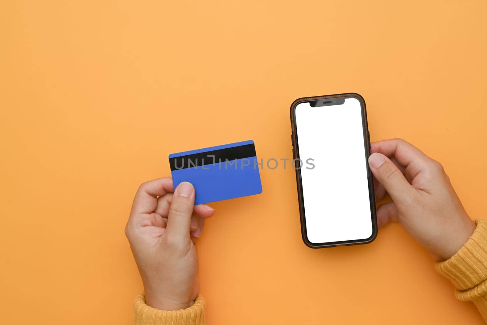 Woman hand holding mobile phone with blank screen and credit card on yellow background.