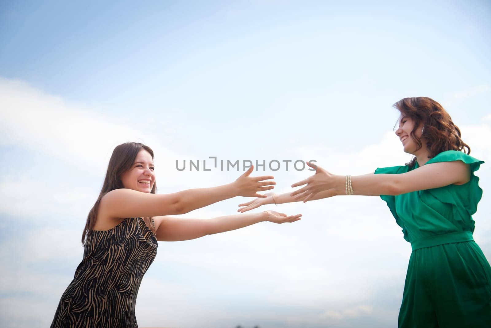 Happy Girls Enjoying Summer Day Together in the Park. Two young women stand on a platform in a park under a bright summer sky, smiling and relaxed