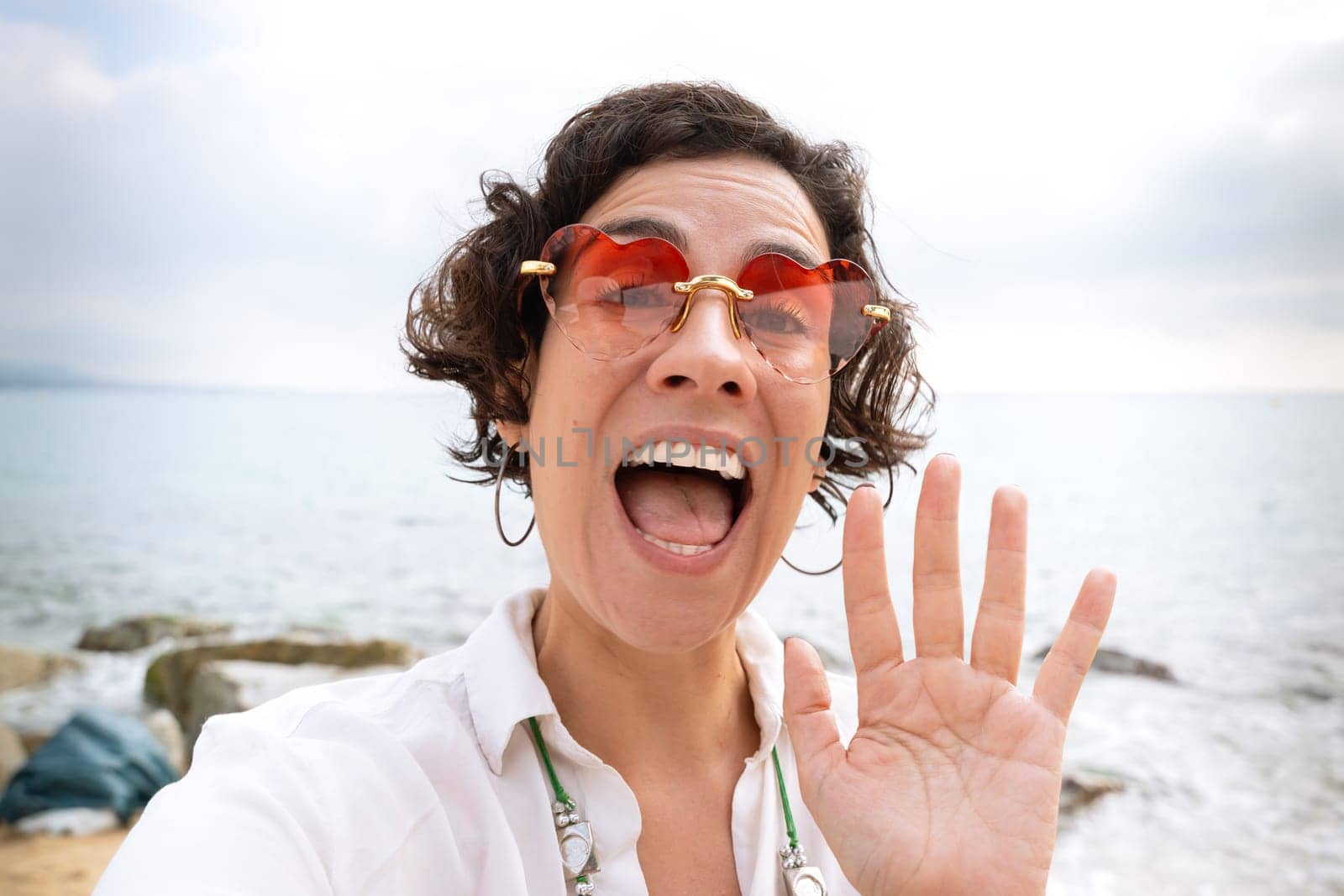 Front view of a caucasian woman wearing sunglasses on vacation by the sea laughing greeting by video call to a family member