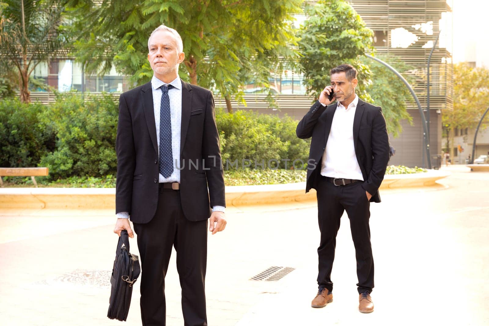 Two businessmen at the exit of a meeting talking on smartphone. by mariaphoto3