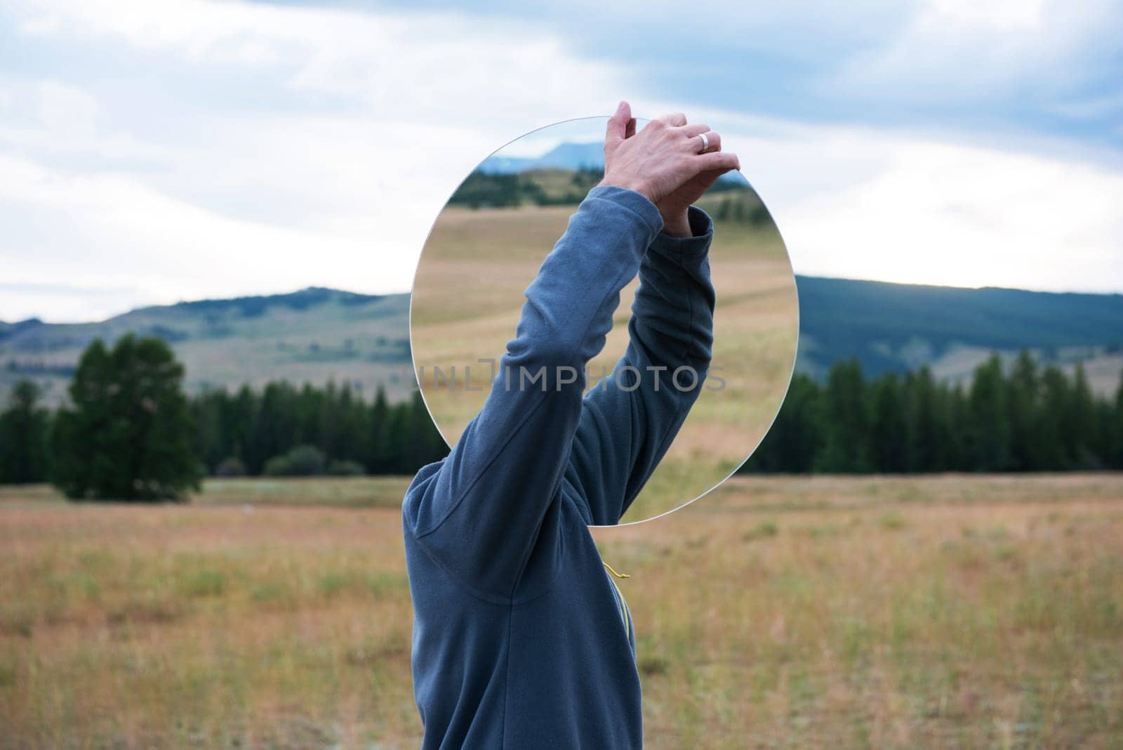 Man standing in in summer Altai mountains in Kurai steppe and holding circle mirror. Creative travel concept