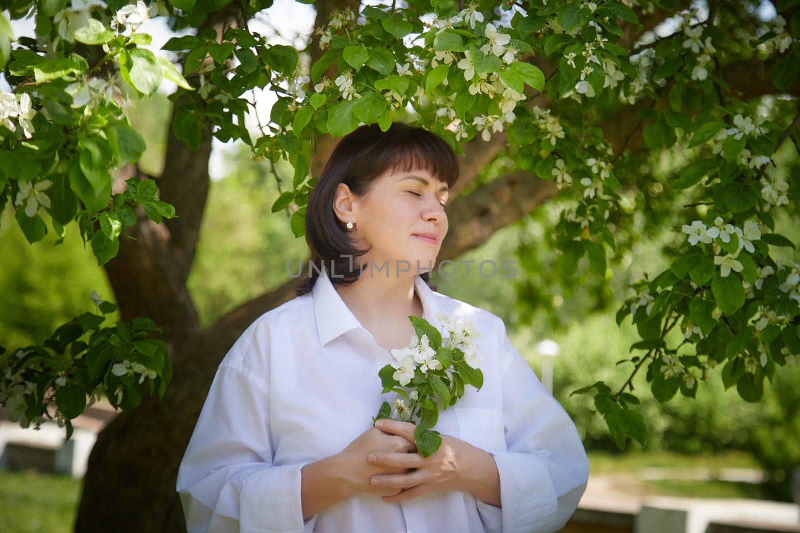 Girl walking, Relaxing near Blossoming apple Tree on Sunny Day. Portrait of Middle aged woman enjoying nature surrounded by white blossoms