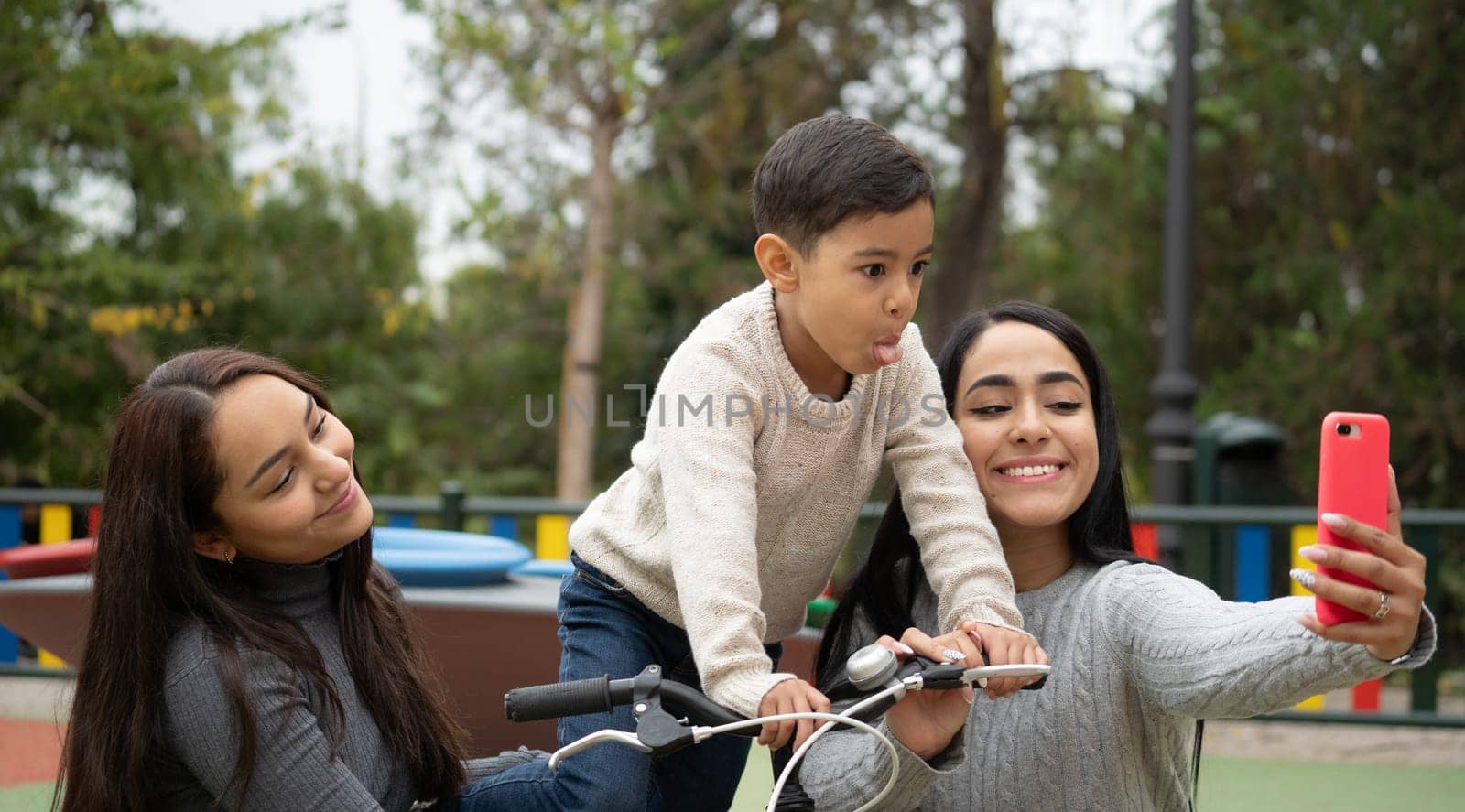 Lesbian mothers taking a funny selfie with her son outdoors in a park. Diversity and LGBT family social inclusion.